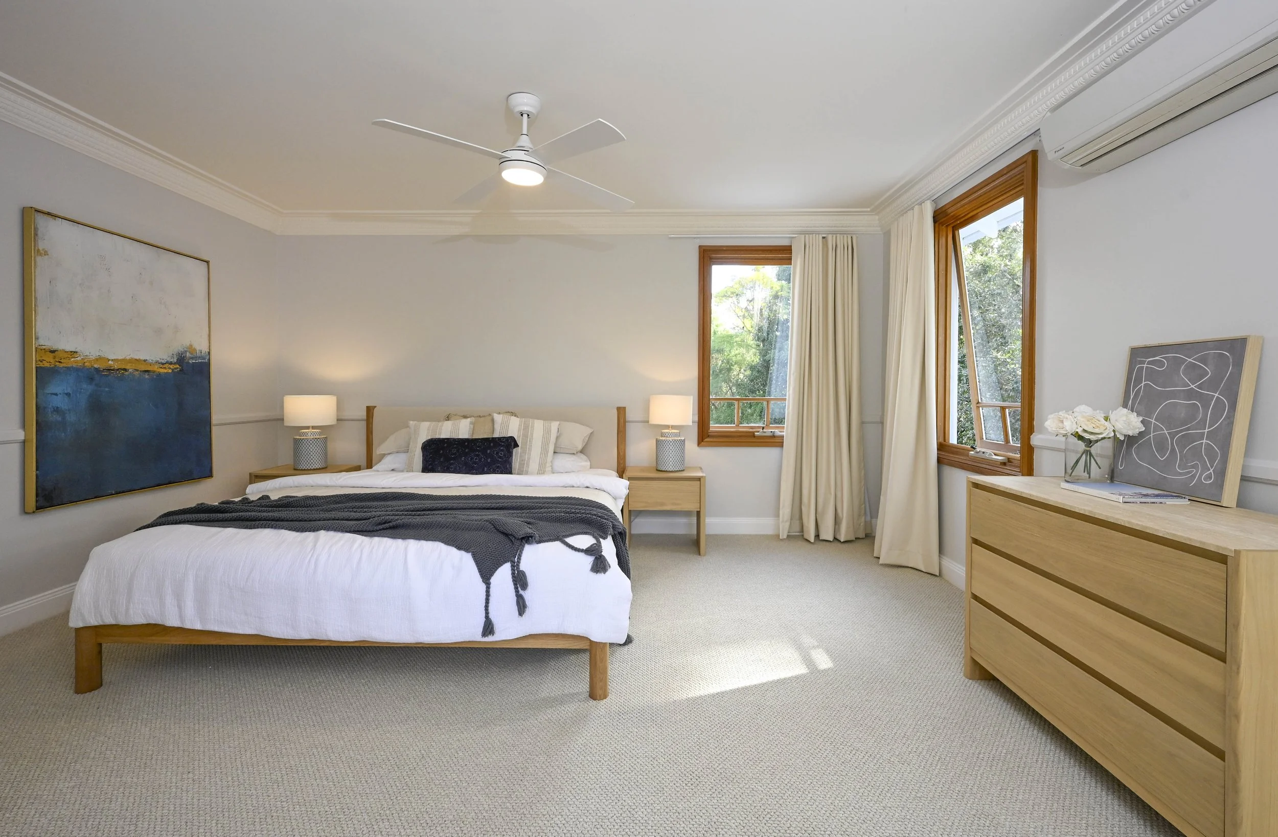 Spacious master bedroom with upholstered bed, neutral styling, soft lighting and cohesive layout in renovated NSW home.