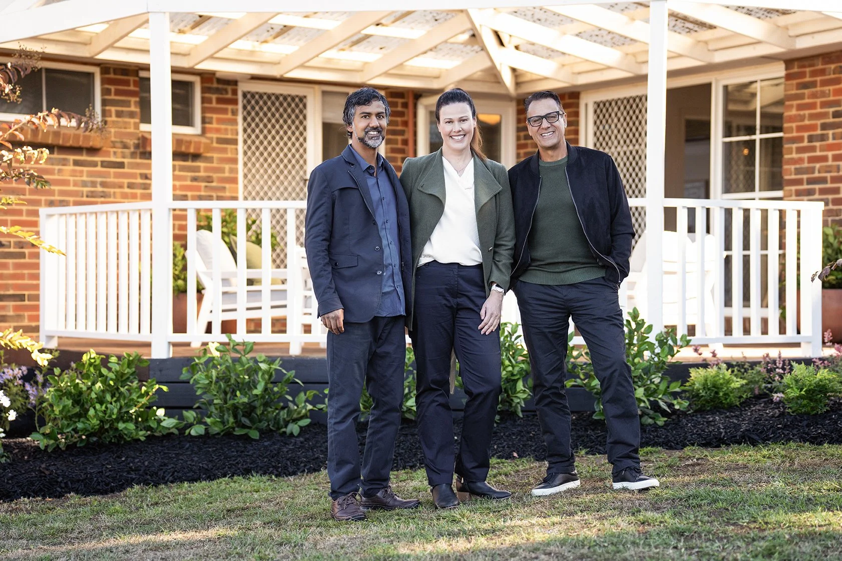 Selling Houses Australia host Andrew Winter with homeowners Jeremy and Lauren smile on the lawn in front of their newly white-painted verandah in Gisborne, Victoria.