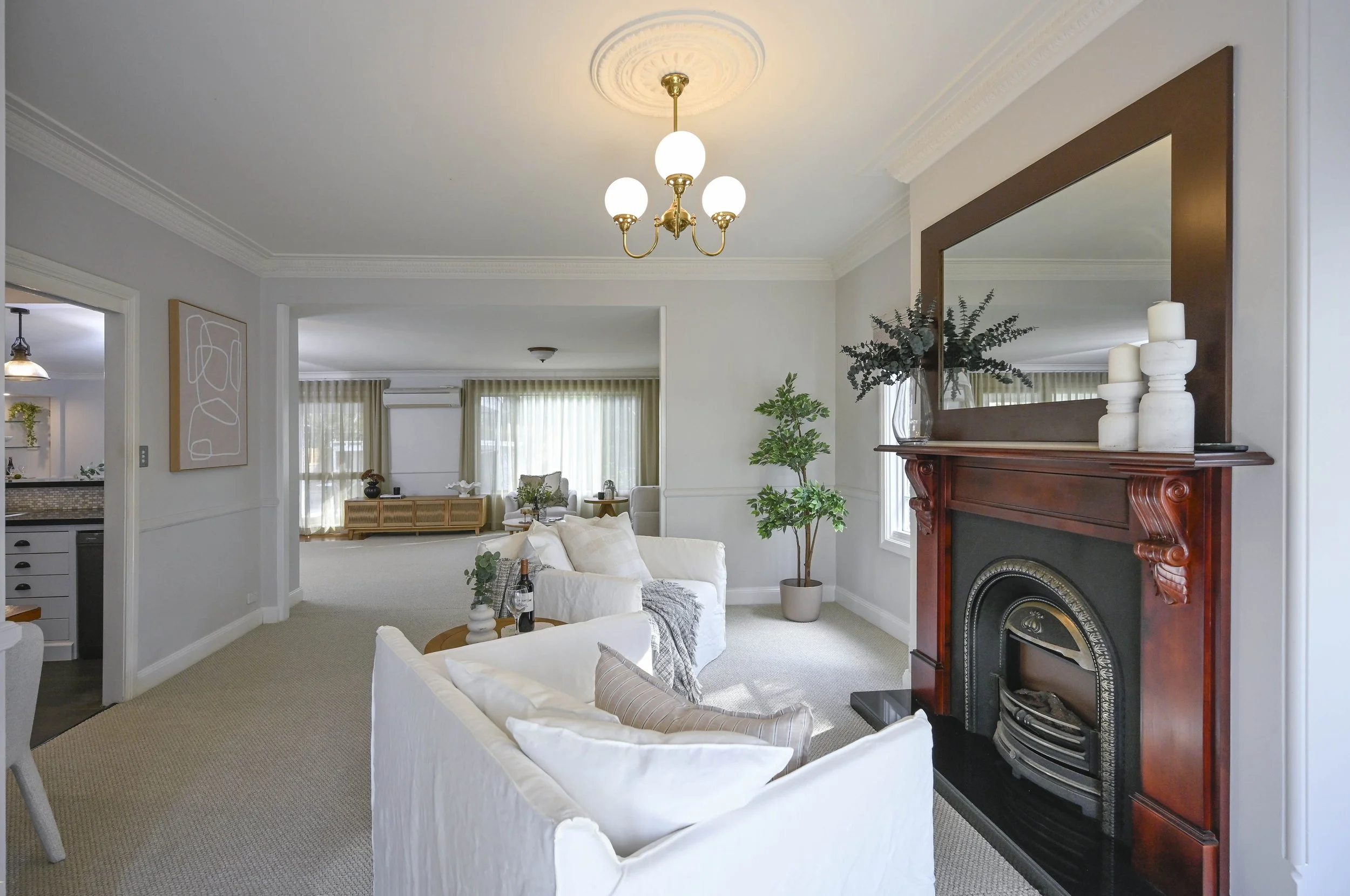 A comfortable living area featuring two white armchairs facing a fireplace with timber surround, decorated in the Cape Cod Hamptons style.