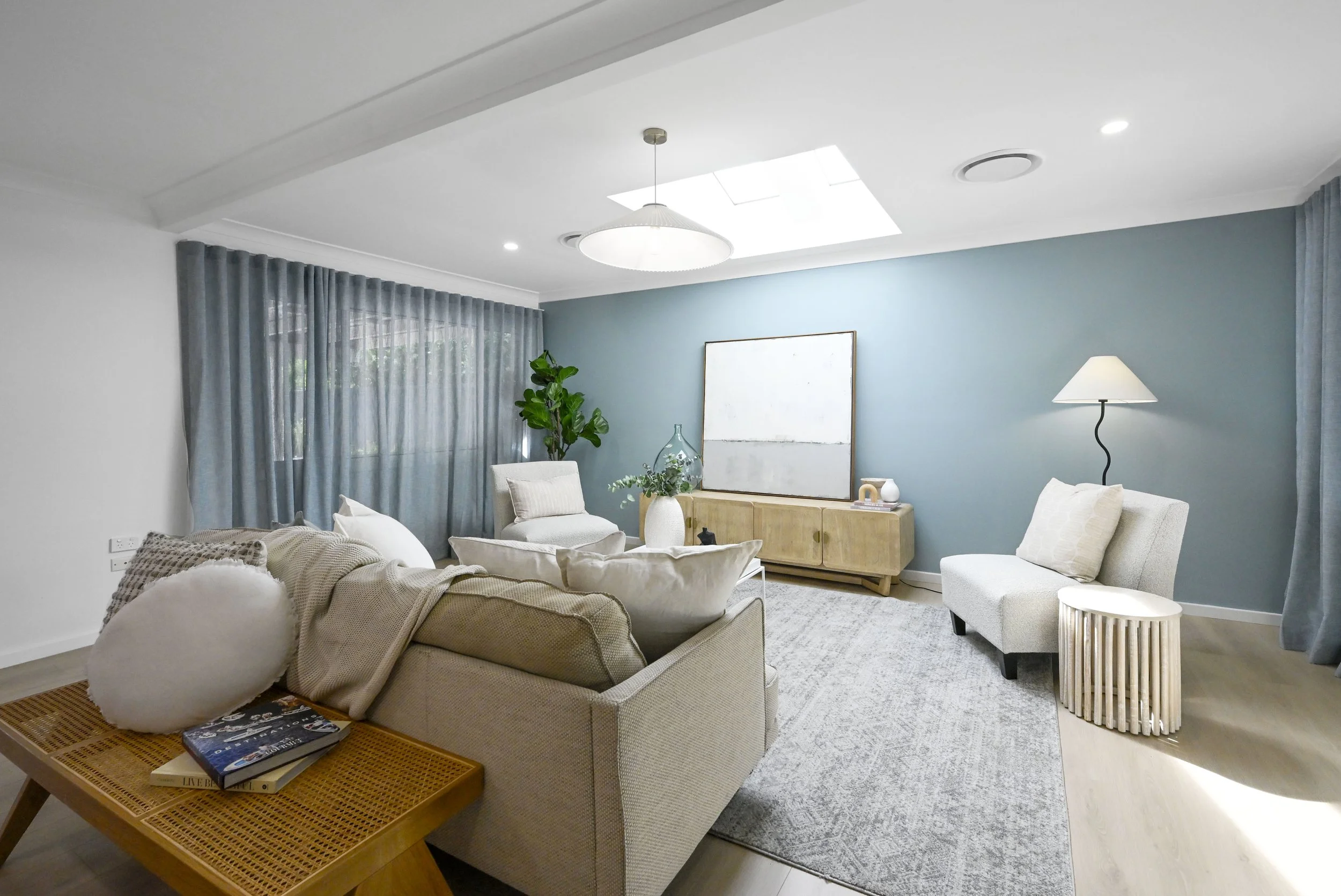 Calm, bright living zone with sheers, layered lighting and coastal styling