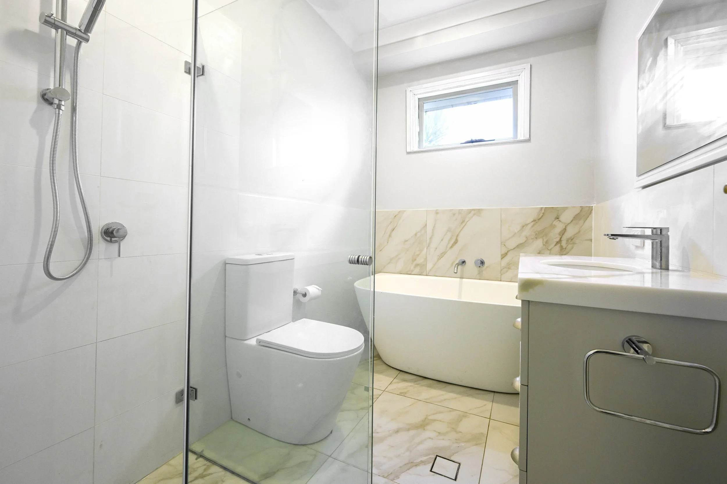 A retiled heritage style bathroom now has a Hamptons vibe, with marble look tiles and white toilet, bath and vanity.