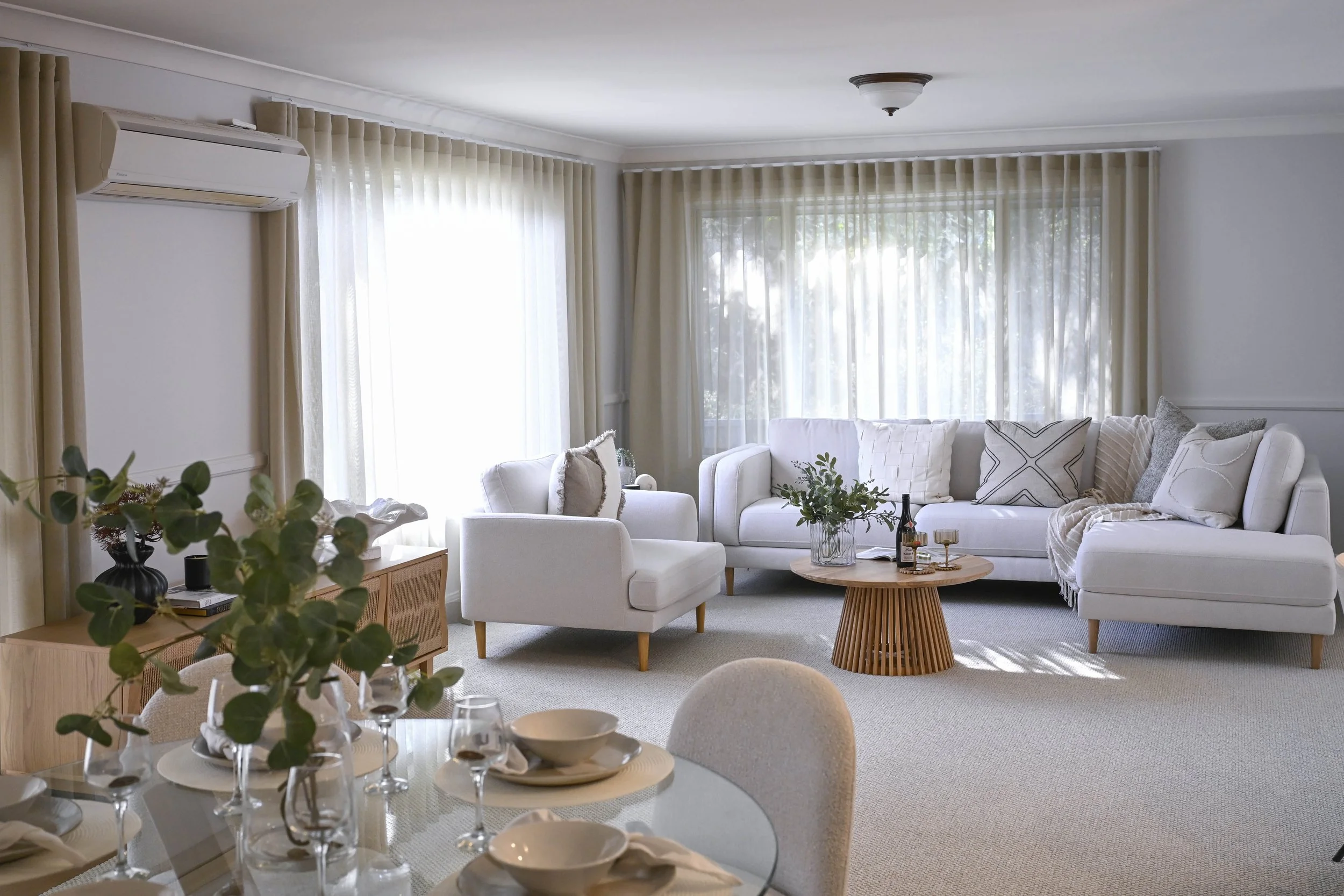 A relaxed Hamptons living room, light filled and bright, with lots of comfortable seating options and a dining zone in the foreground.