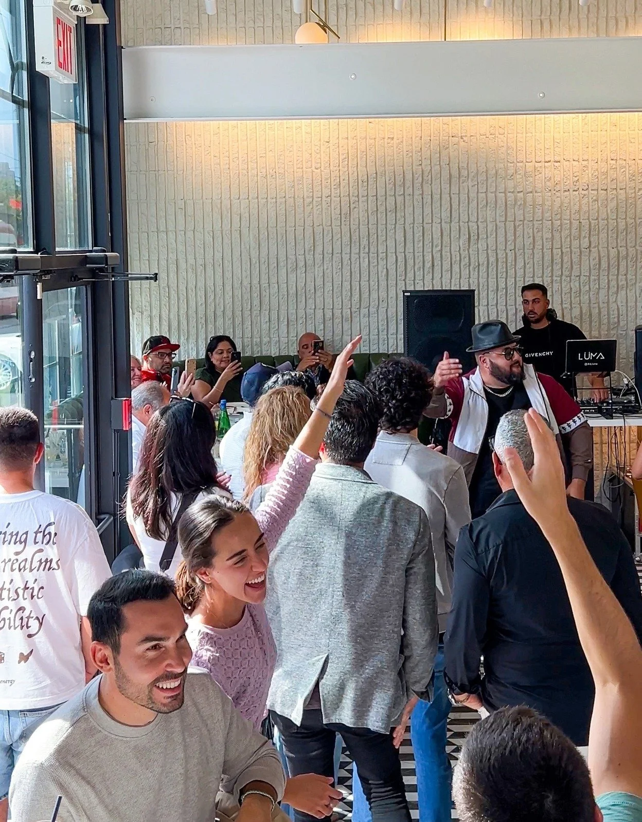 A lively indoor gathering with people dancing and enjoying music, led by a DJ at the turntables.