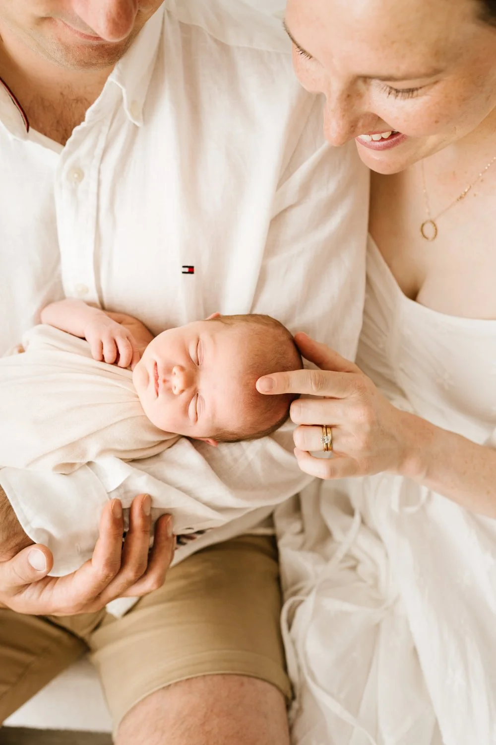 A newborn baby sleeping peacefully, being cradled by parents who are smiling and looking at the baby affectionately.