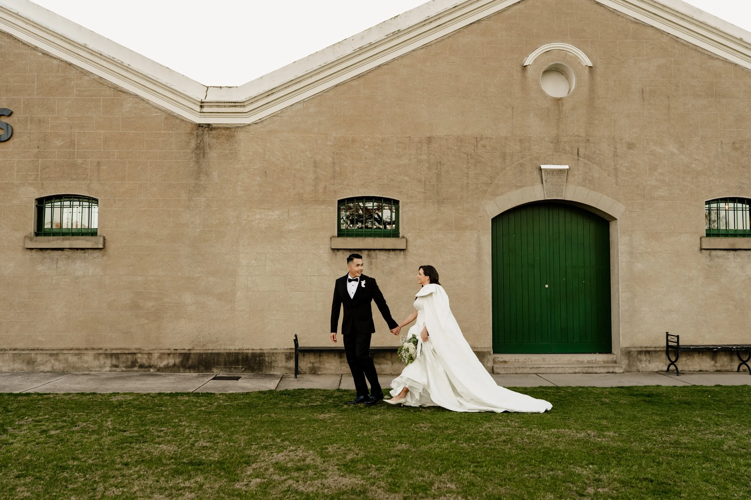 Bride and groom walking along grass in front of building