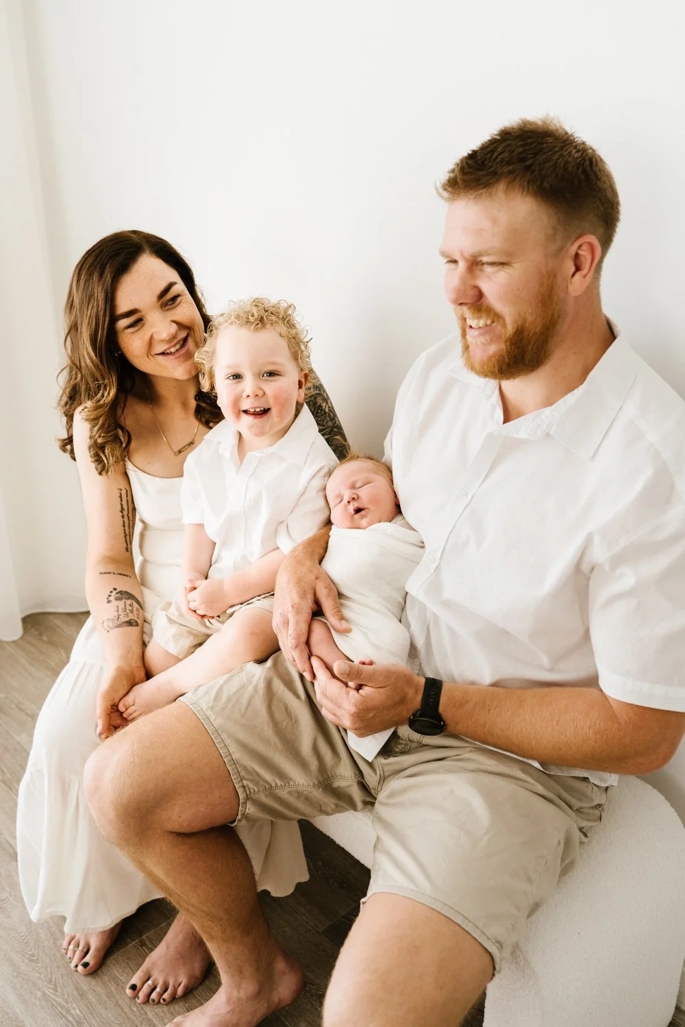 A happy family with four members, including a woman, a man, a young boy, and a newborn baby, sitting together indoors.