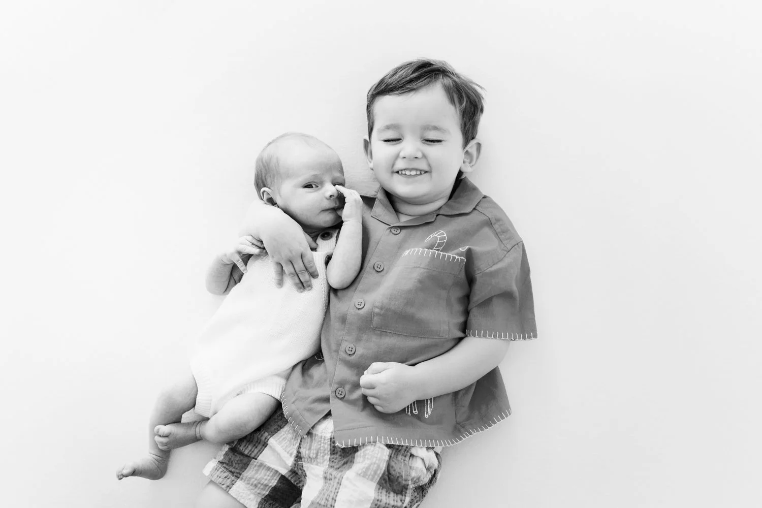 A young boy sitting with a baby, both smiling, in black and white photo.
