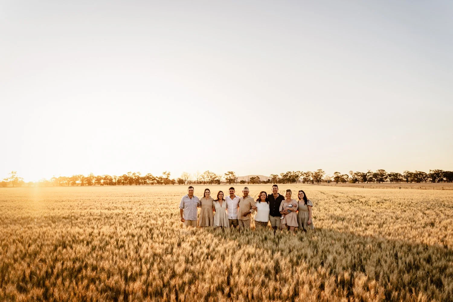 Large family standing in a wheat field looking at the camera as the sun sets