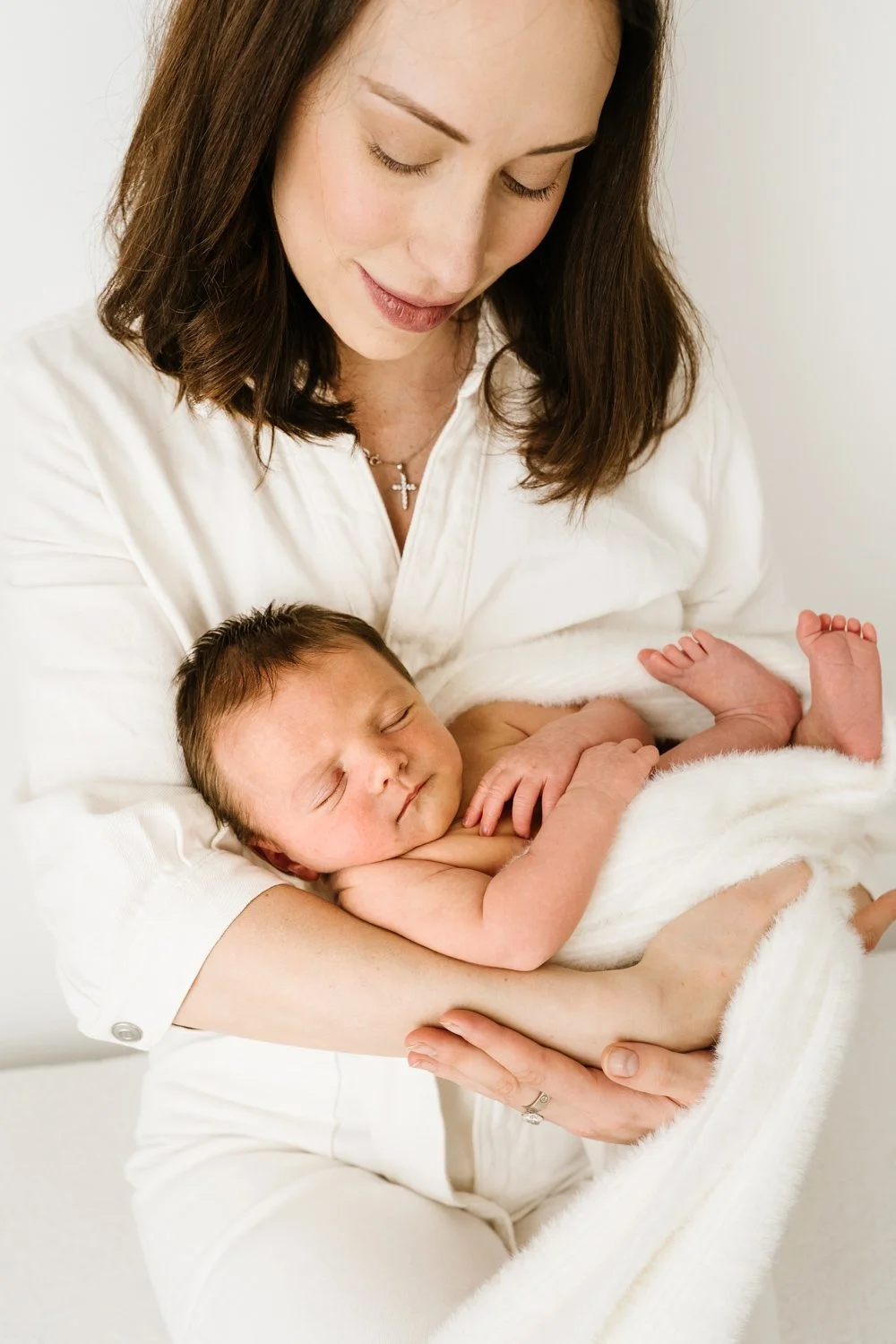 A woman holding a sleeping newborn baby wrapped in a white blanket.