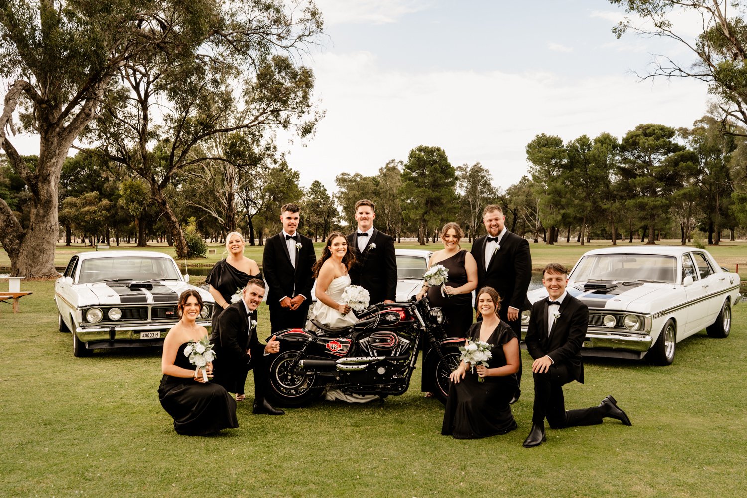 everyone in the wedding party gathers around the bride and groom as they sit on a motorbike