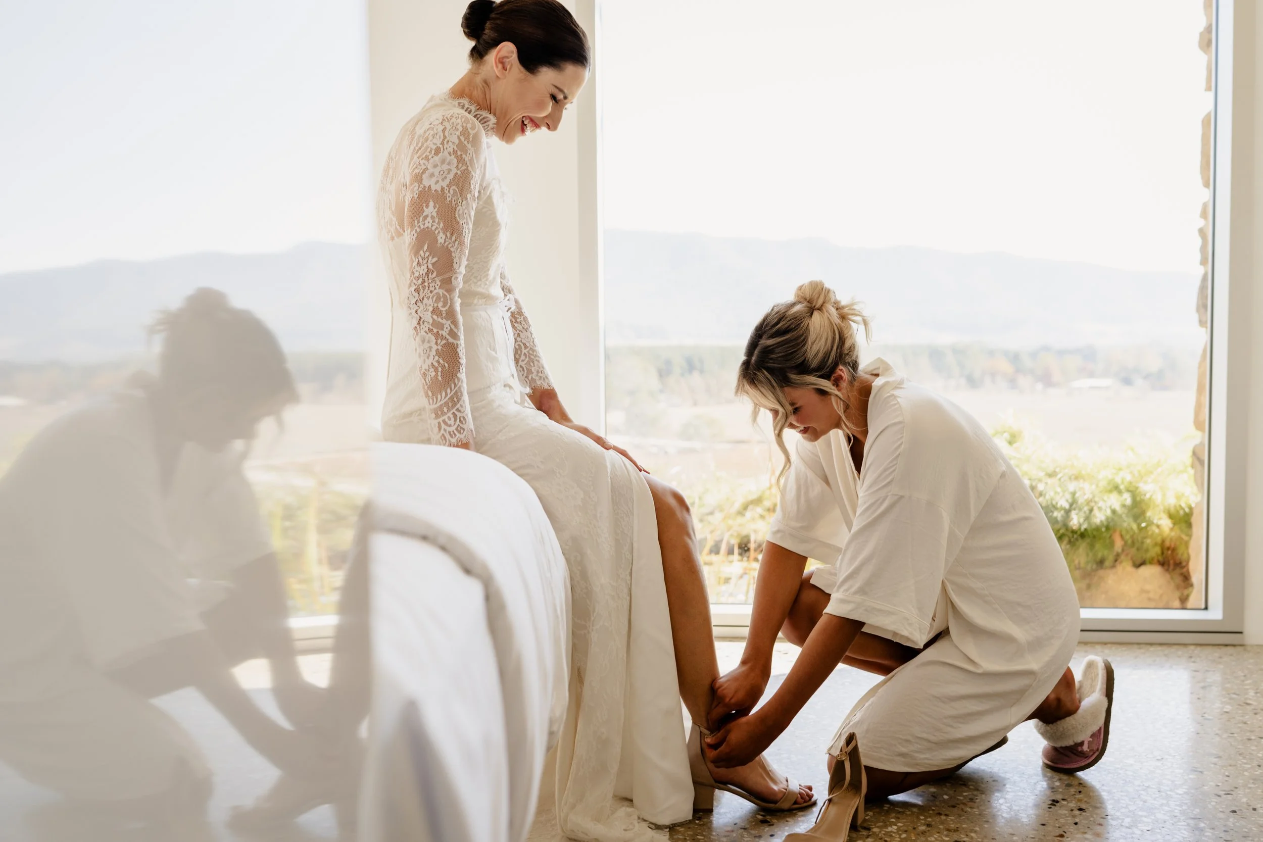 Bridesmaid helping bride put on shoes