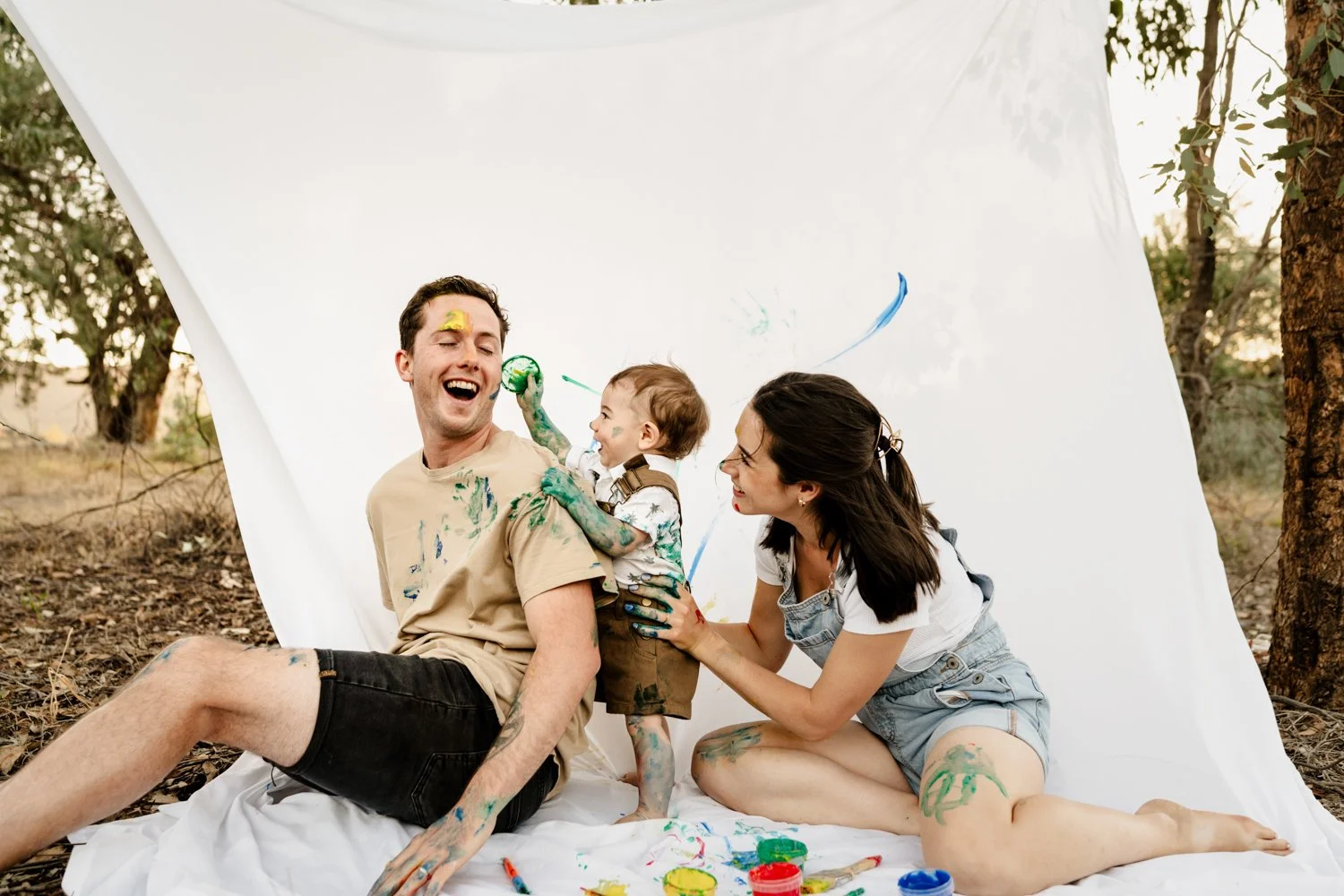 little boy paints his dads face with a paint brush playfully