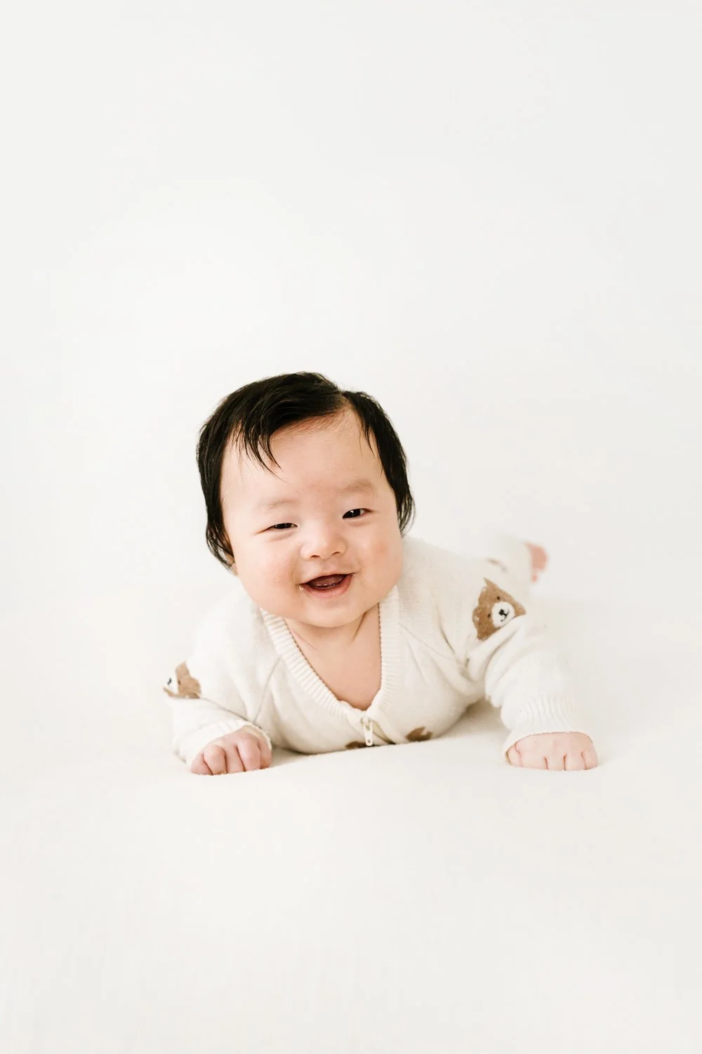 Smiling baby crawling on a white surface with a white background.