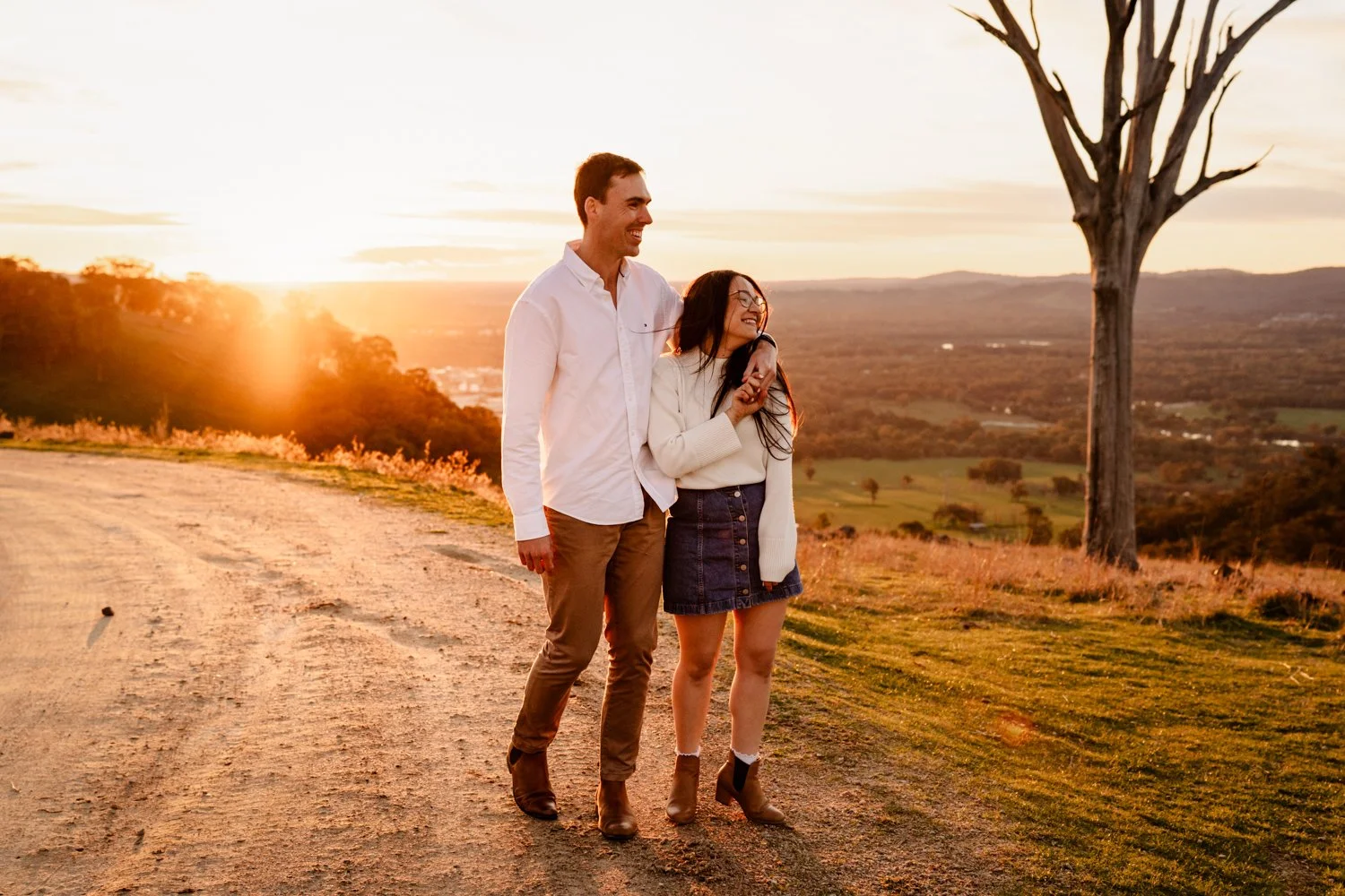 A newly engaged couple walking together holding hands at sunset