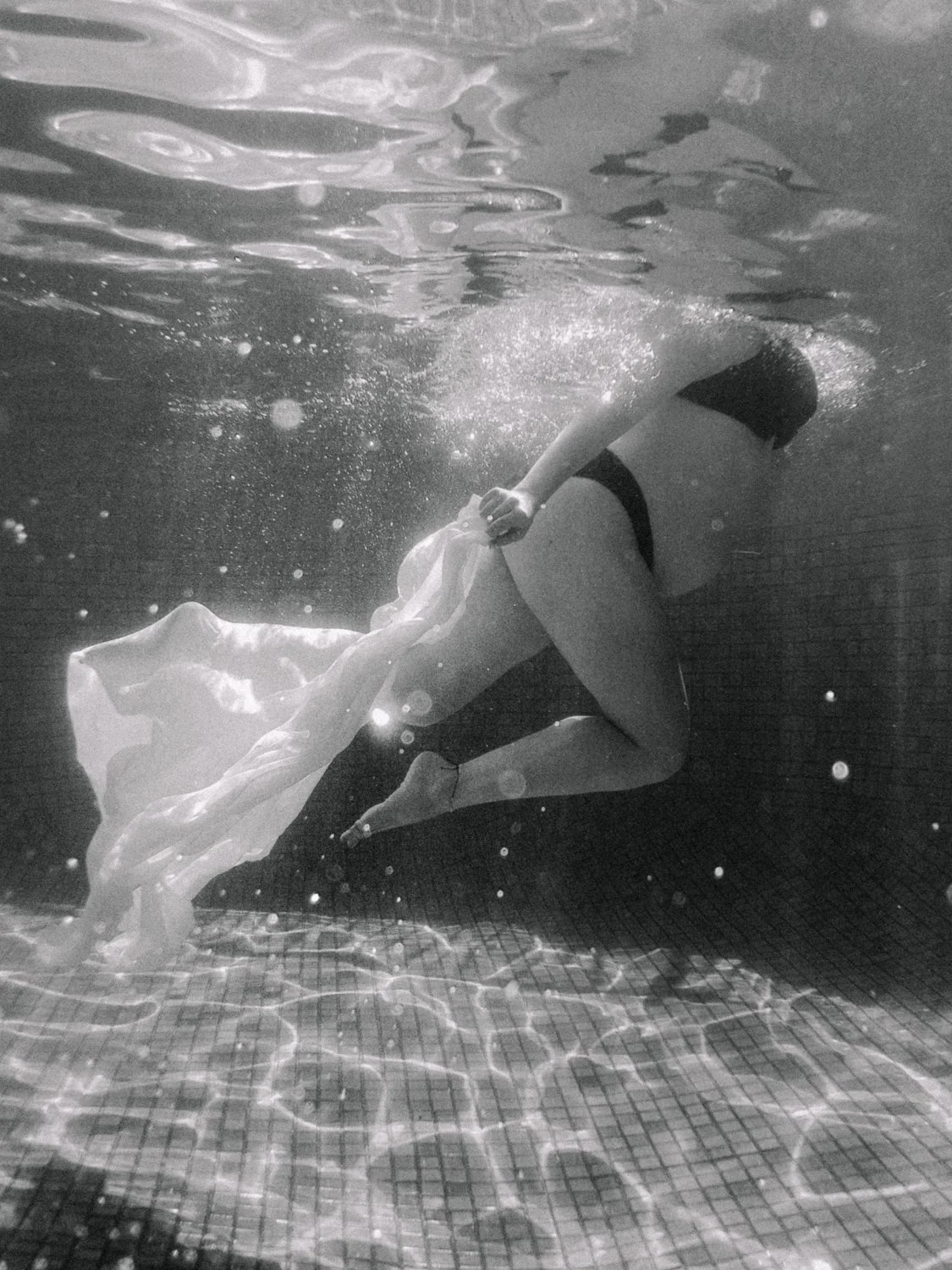 A person underwater in a swimming pool holding a flowing piece of fabric.