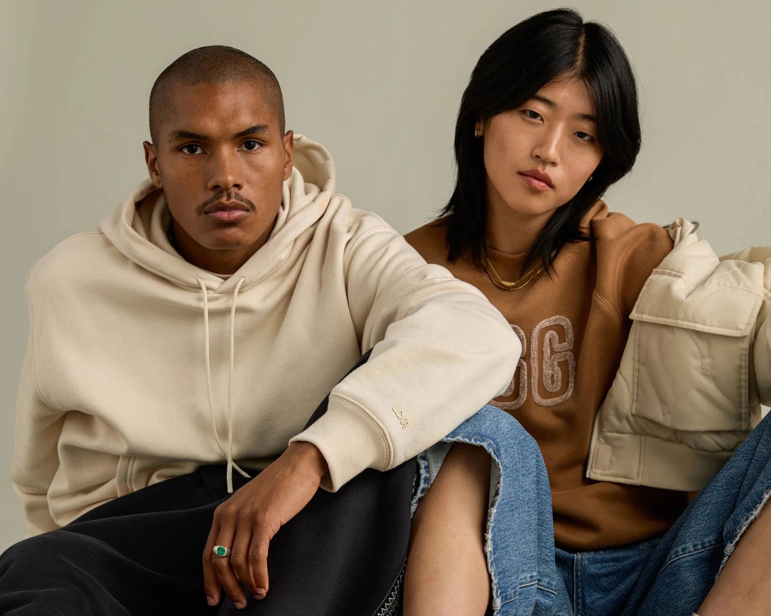 A man and woman sitting close together against a plain wall, wearing casual clothing, with neutral expressions.