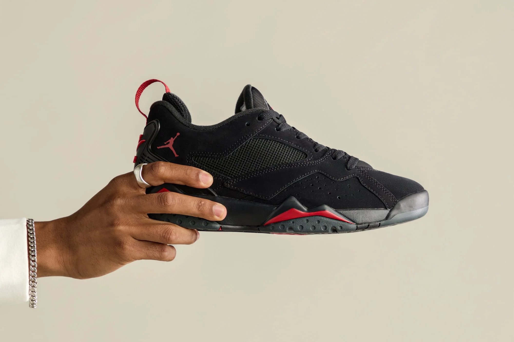 Person holding a black and red Nike Air Jordan sneaker against a plain beige background.