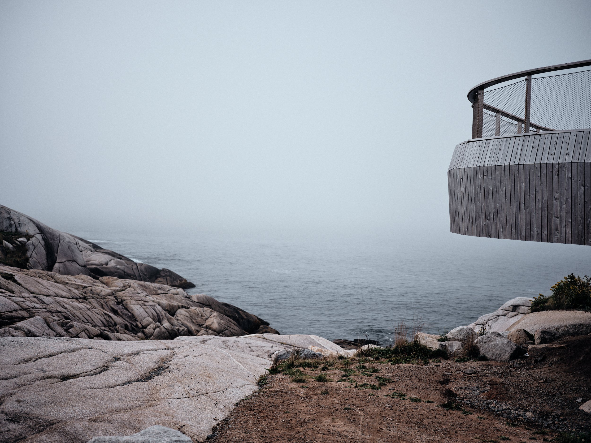 Foggy coastal scene with rocky shoreline and water, featuring a large wooden deck or observation platform on the right side.