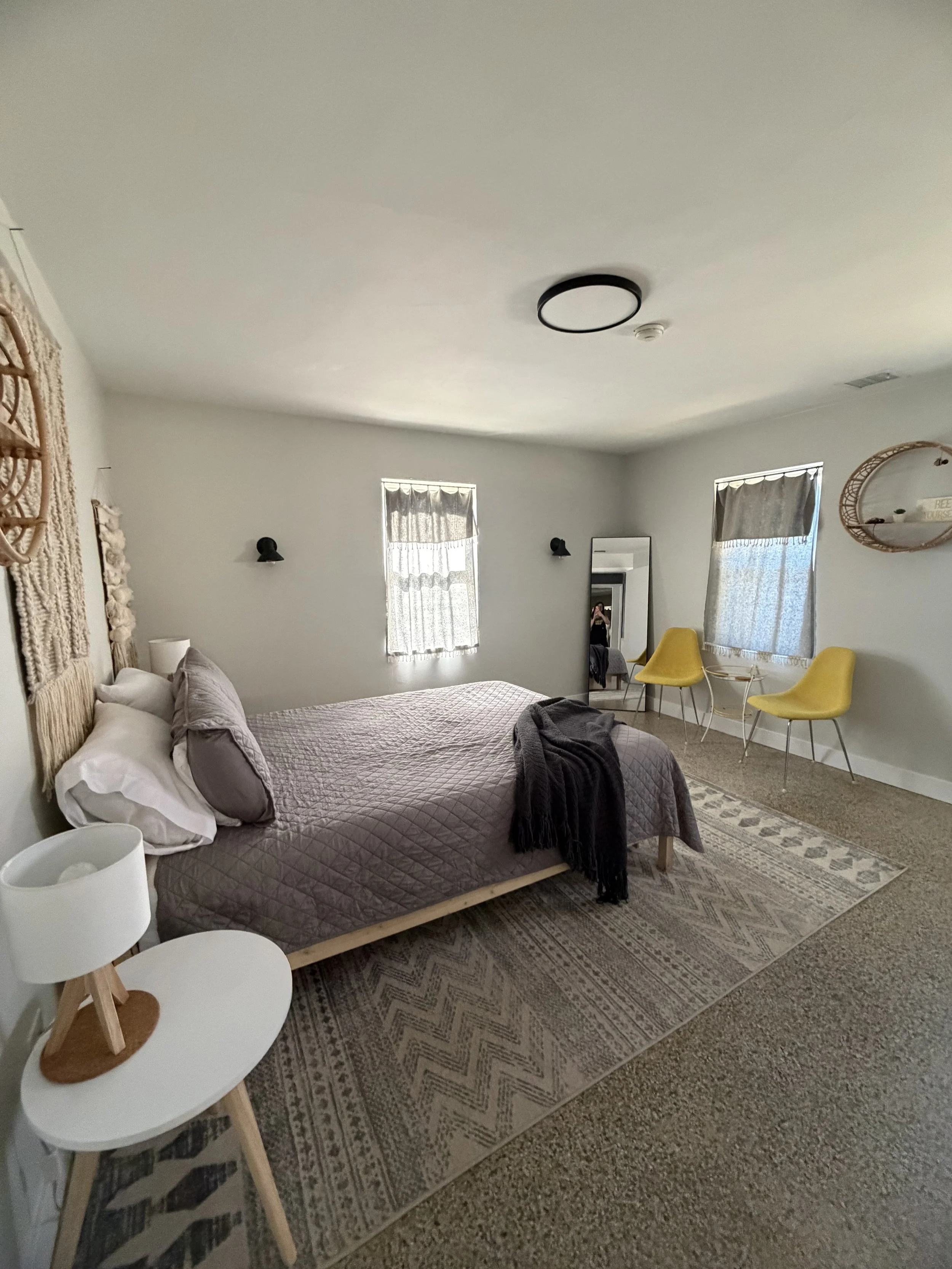 A bedroom with a bed, yellow chairs, a mirror, and decorative wall hangings.