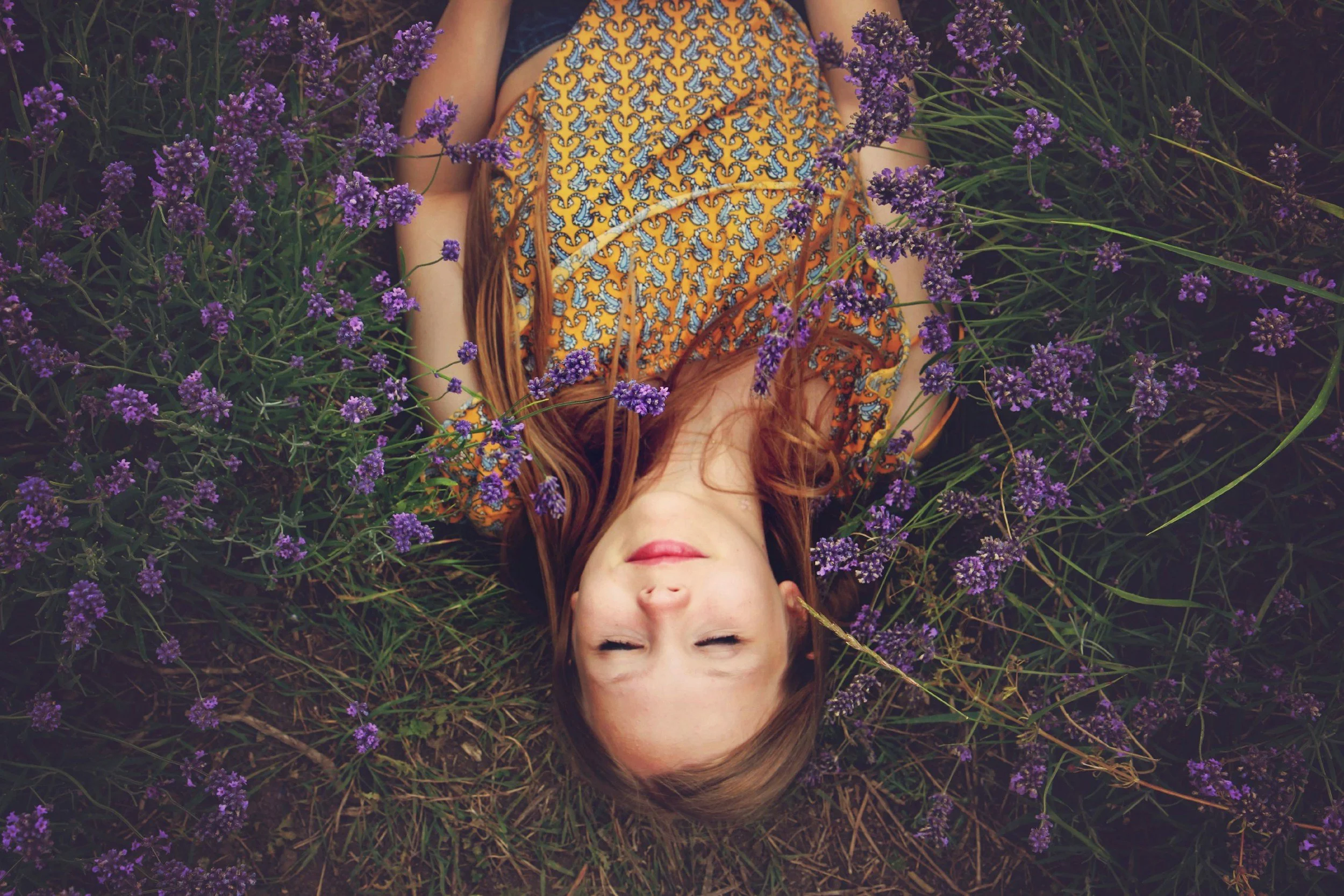 A peaceful child lying in a lush field of green grass and blooming purple flowers, illustrating inner child healing through IFS therapy in Kansas City area.