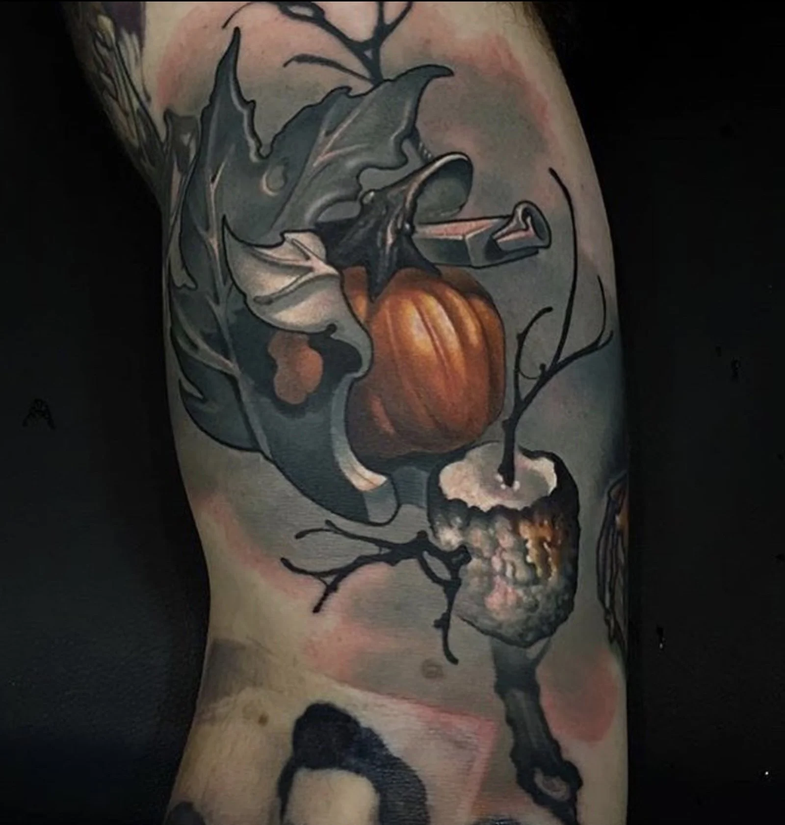 Colorful tattoo of a pumpkin, leaves, and branches on a person's arm.