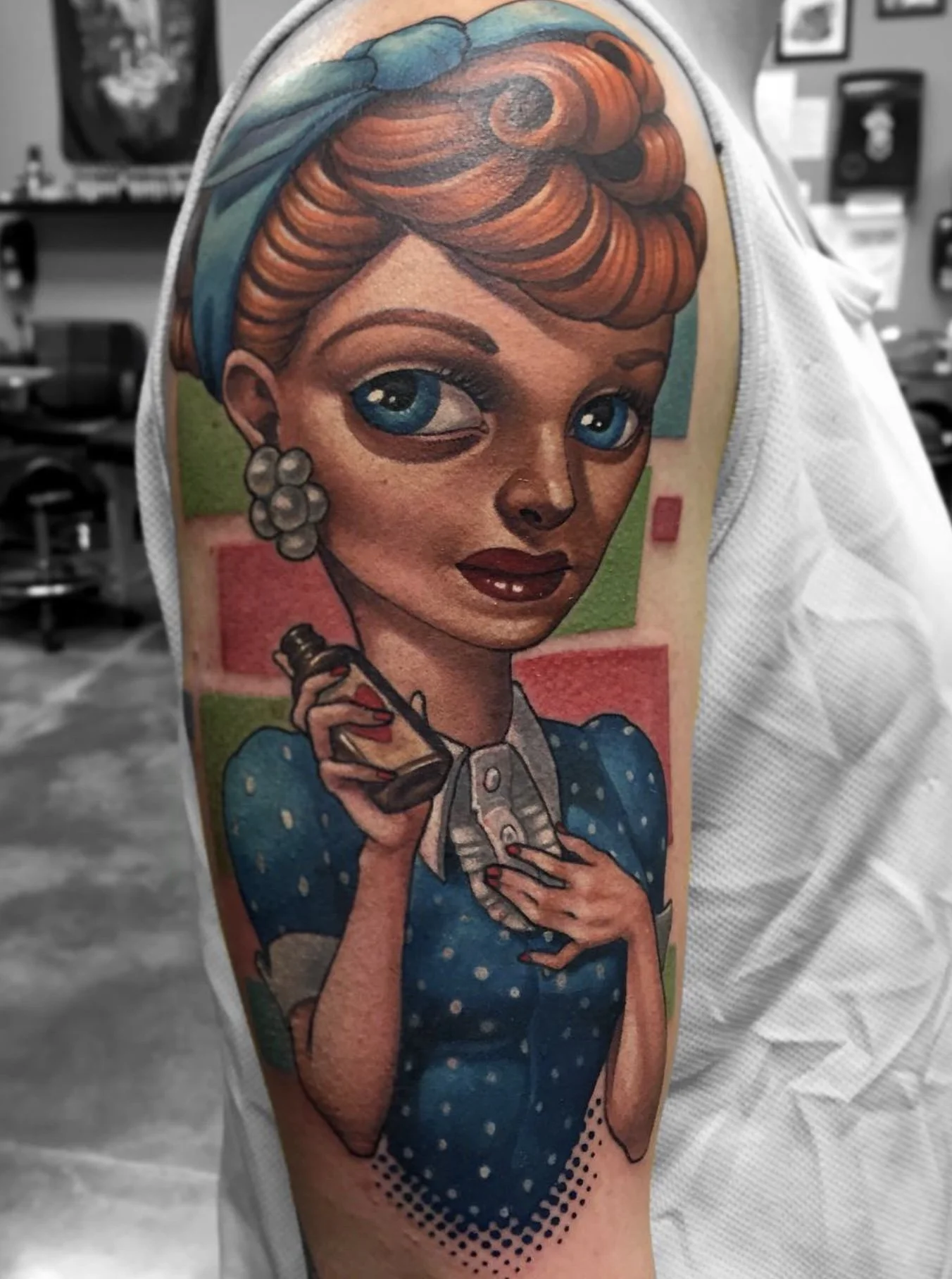Colorful tattoo of a woman with blue eyes, red hair styled in waves, earrings, and holding an old-fashioned telephone, in a vintage comic book style on someone's upper arm.