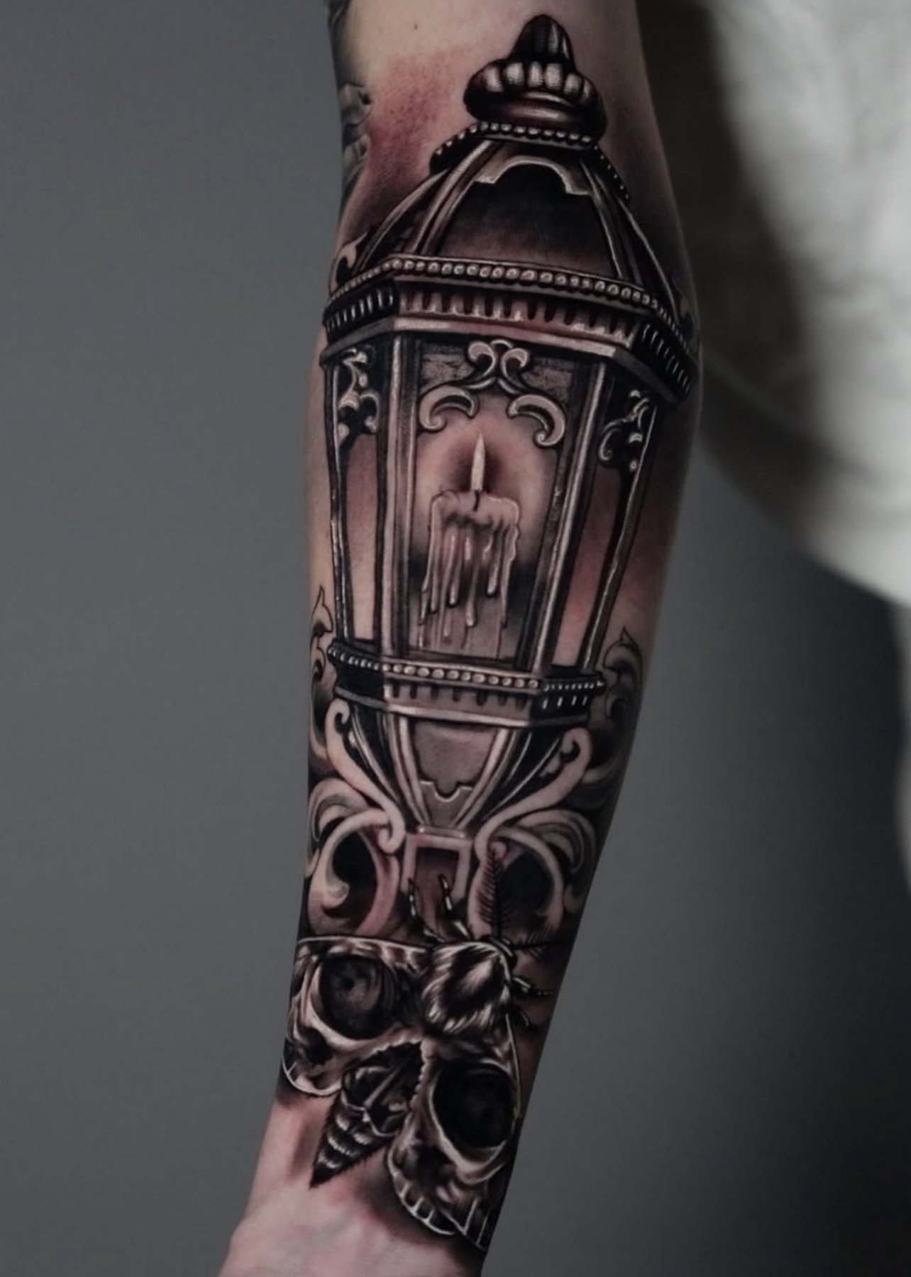 Black and gray tattoo of a birdcage with a lit candle inside, dripping wax, and a skull at the bottom of the design on a person's forearm.
