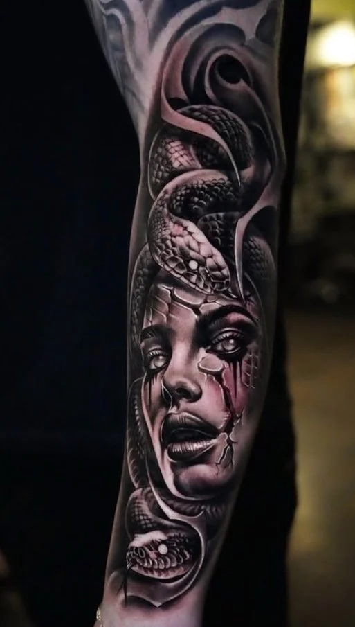 Black and gray tattoo of a woman's face with a snake intertwined around her head, with cracked skin details.