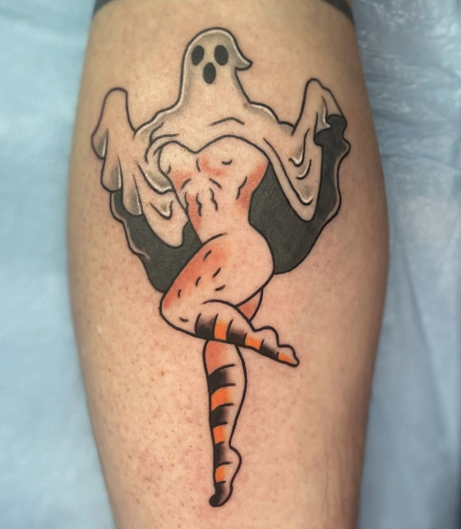 Tattoo of a ghost with a surprised expression and a tongue sticking out, with a forked tongue and orange and black striped tail.
