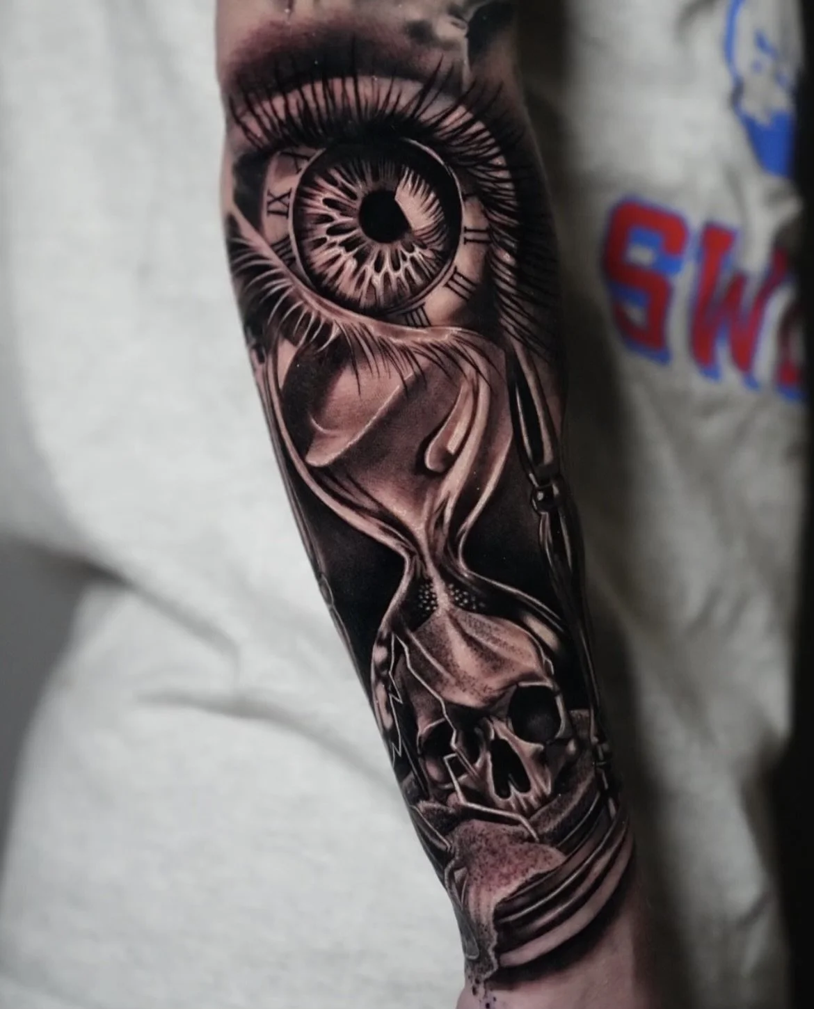 Tattoo of an eye with clock elements, a skull, and flowing lines on a person's forearm.