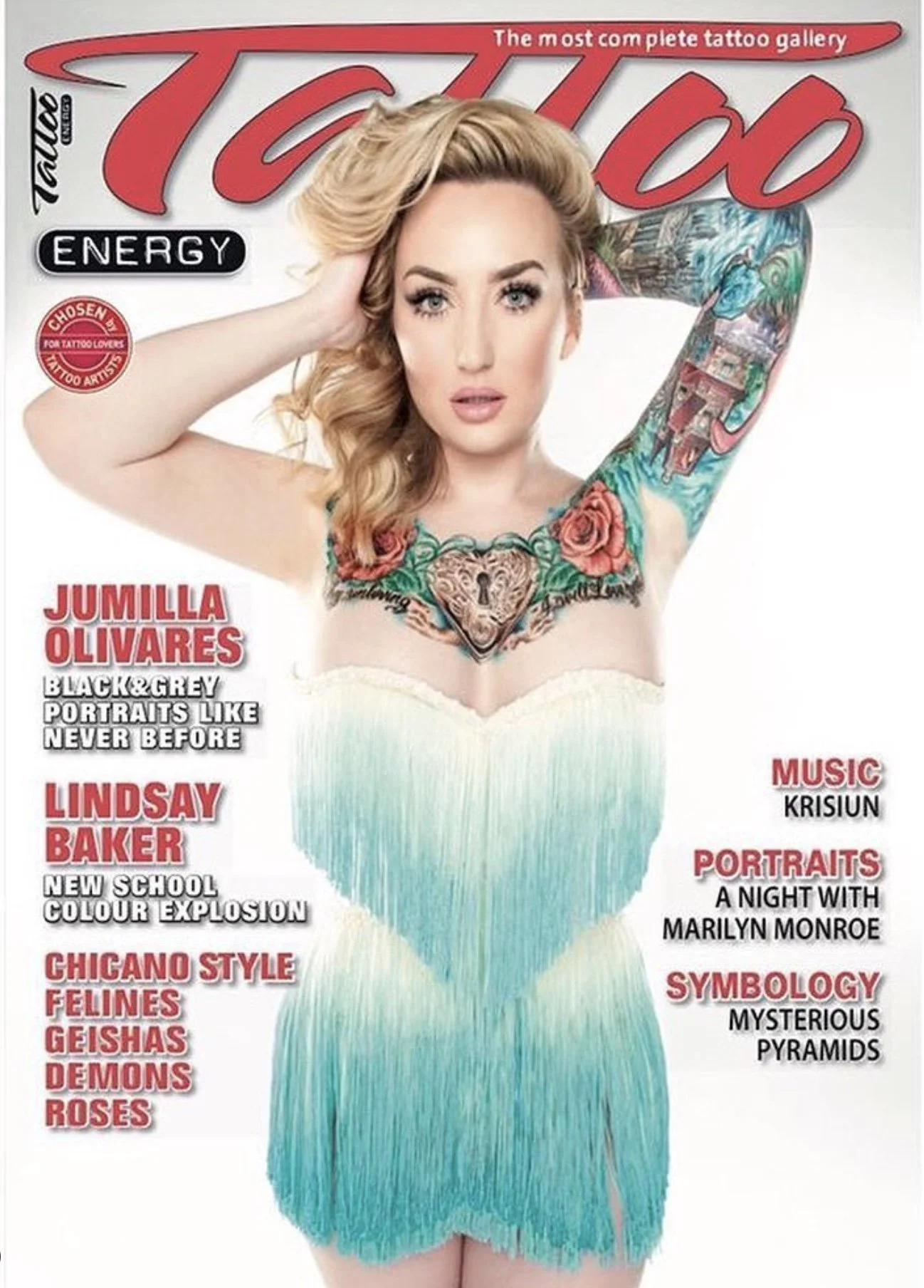 A woman with blonde hair and tattoos on her right arm and chest, wearing a strapless dress with a gradient from white to blue.