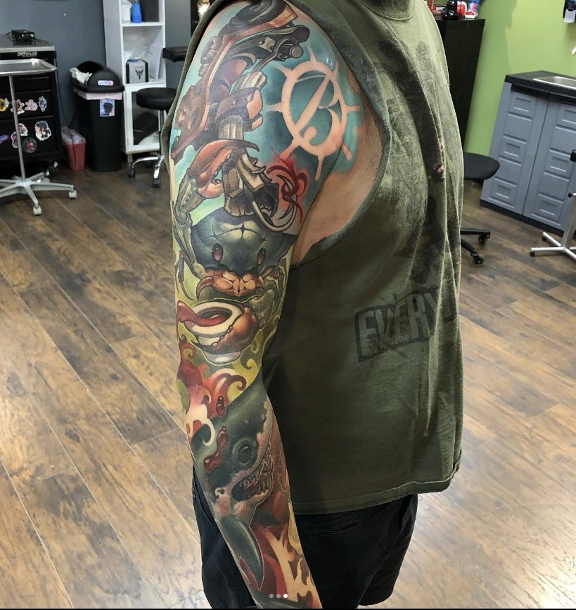 A colorful full-arm tattoo featuring a crab, a crab-themed face, a demonic creature, and various abstract designs on a person's arm.