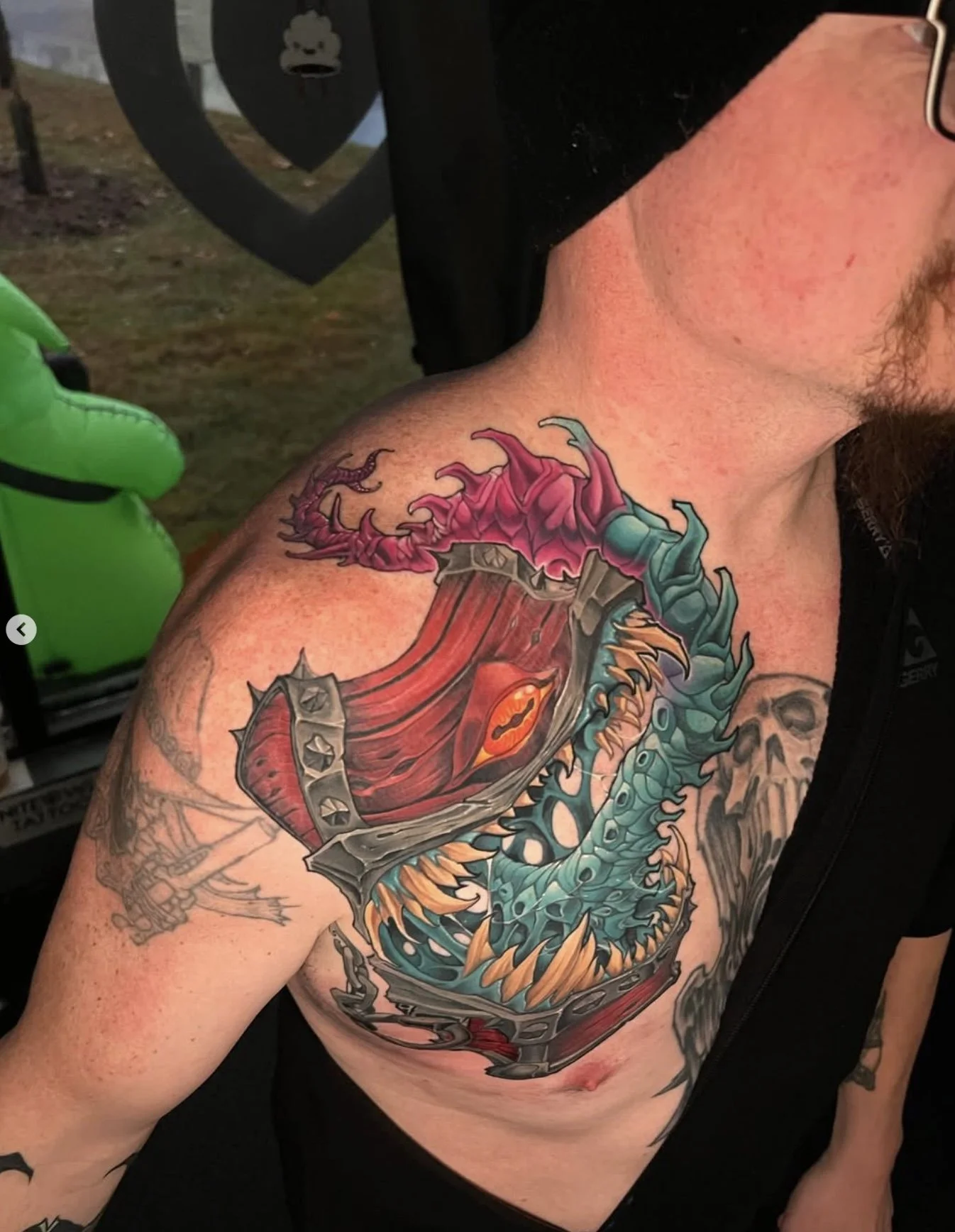 A colorful dragon tattoo on a man's shoulder and chest, featuring a blue-green body with orange spikes and a red, open mouth with sharp teeth.