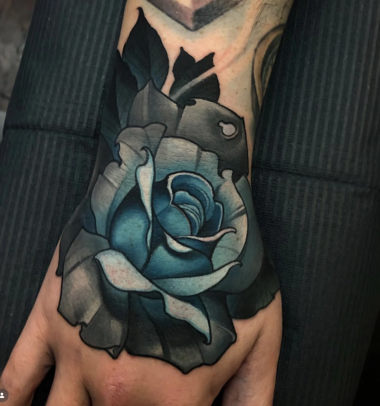 A tattoo of a blue rose with green leaves and a black ribbon is inked on a person's upper arm.