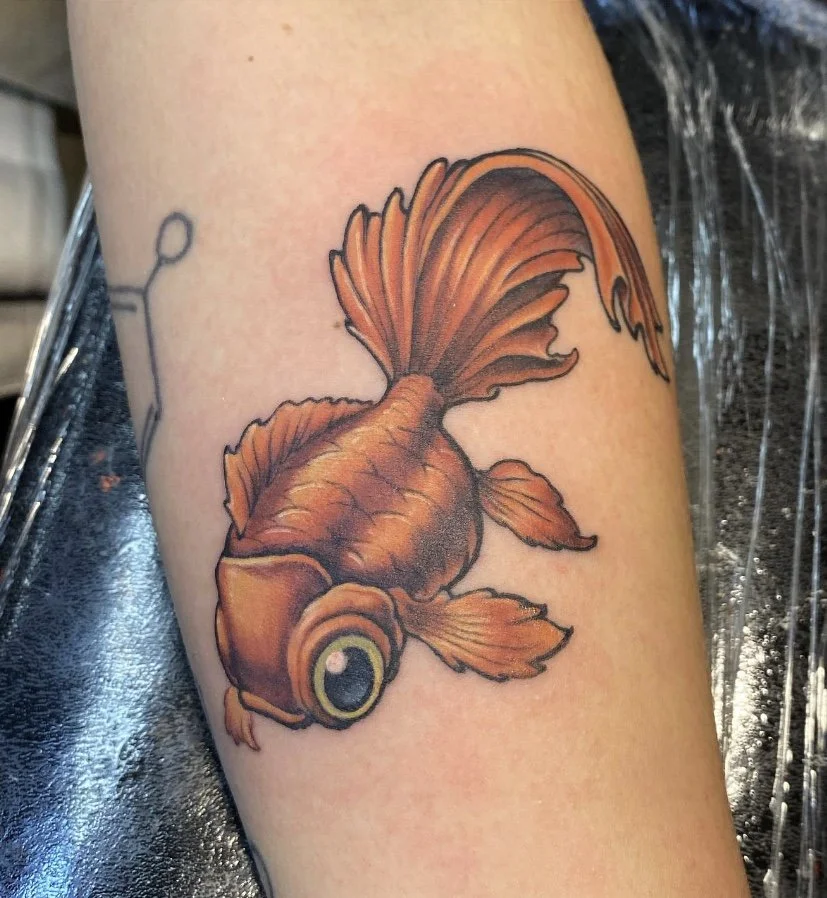 A colorful tattoo of a goldfish with flowing fins on a person's arm.