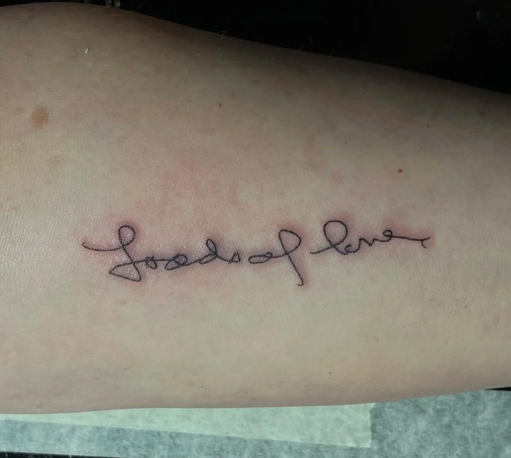 A close-up of a person's skin with the words 'good love' tattooed in cursive, dark ink.