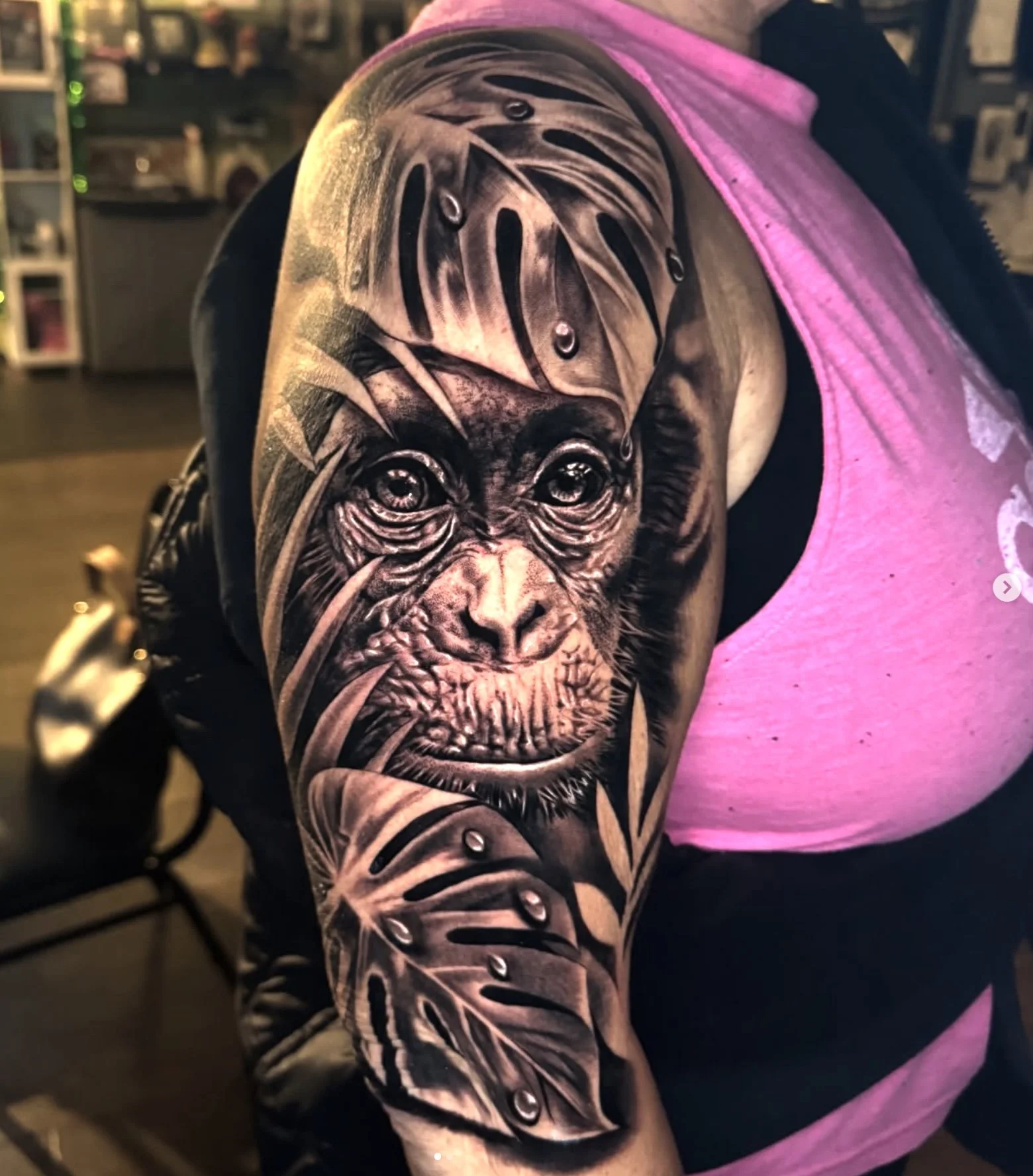 Black and gray tattoo of a monkey's face on a person's upper arm, with monkey's face detailed and realistic, surrounded by abstract leaves and patterns.