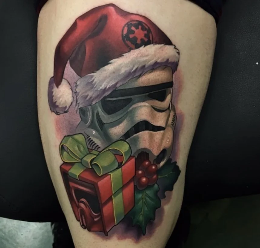 Tattoo of a stormtrooper helmet from Star Wars wearing a Santa hat, with a Christmas gift box, holly, and berries.