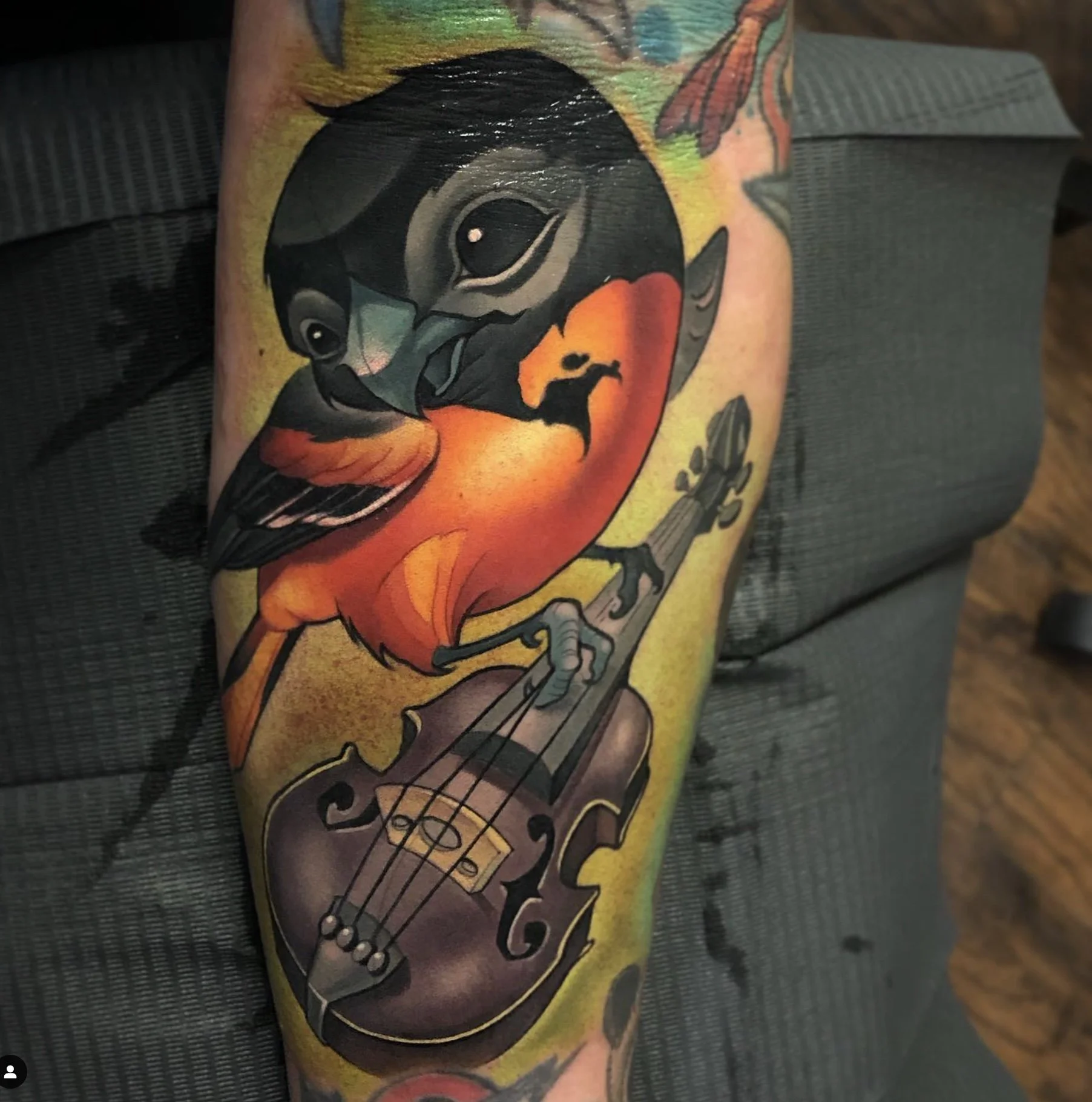 Colorful tattoo of a bird with a guitar body on a person's arm.