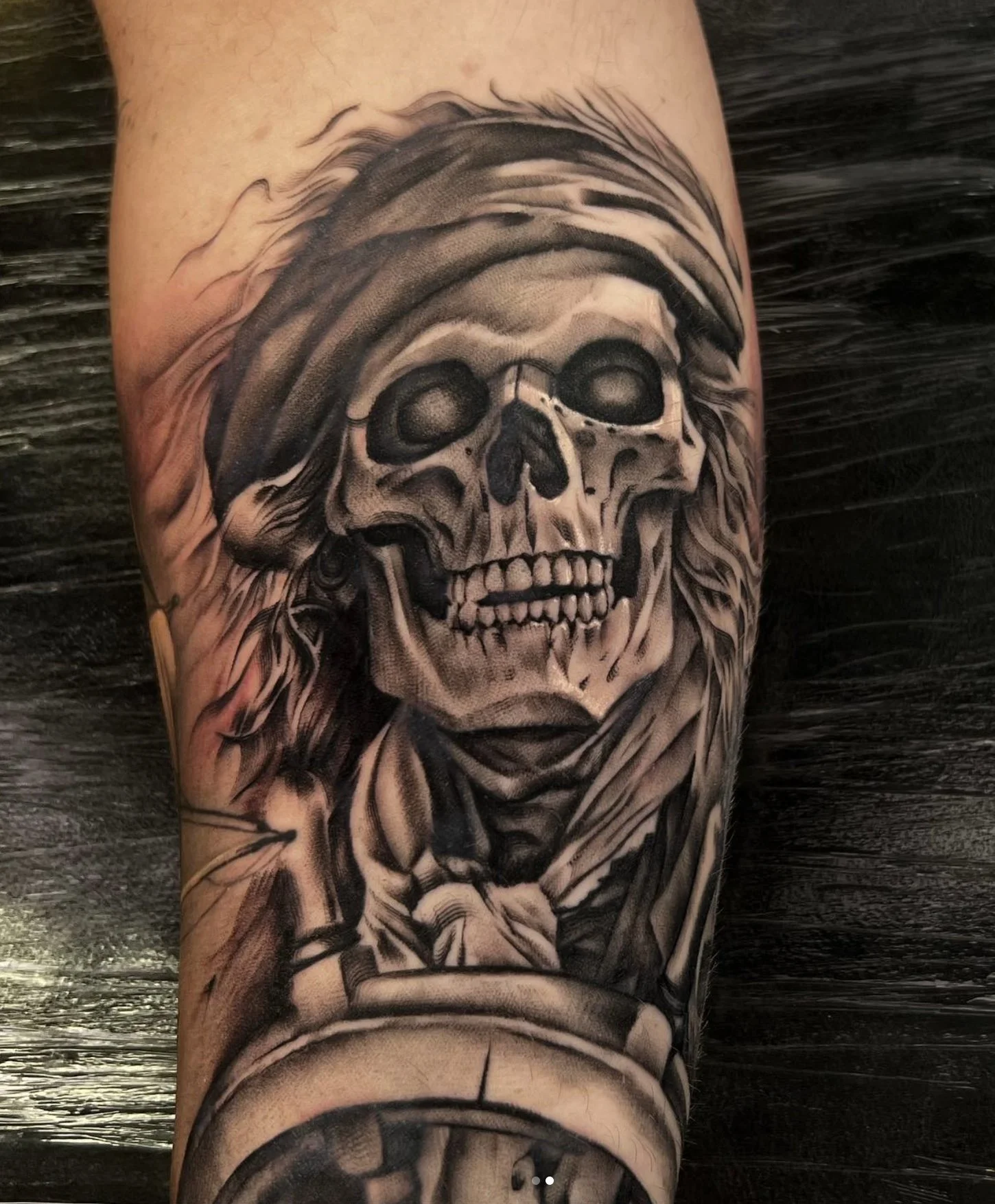 Tattoo of a skull wearing a pirate hat and a bandana on a person's arm.