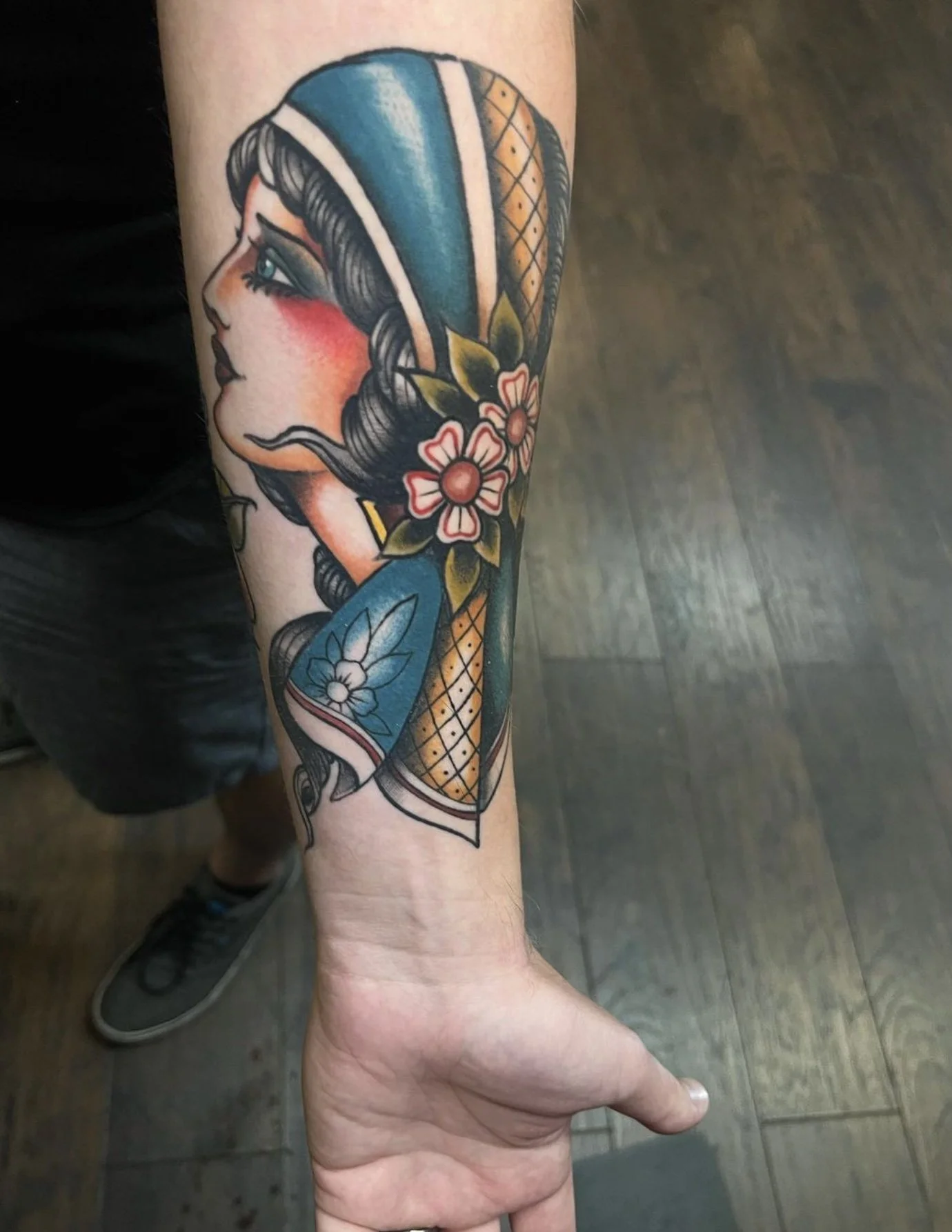 Tattoo of a woman with blue hair, flowers, and geometric patterns on arm.