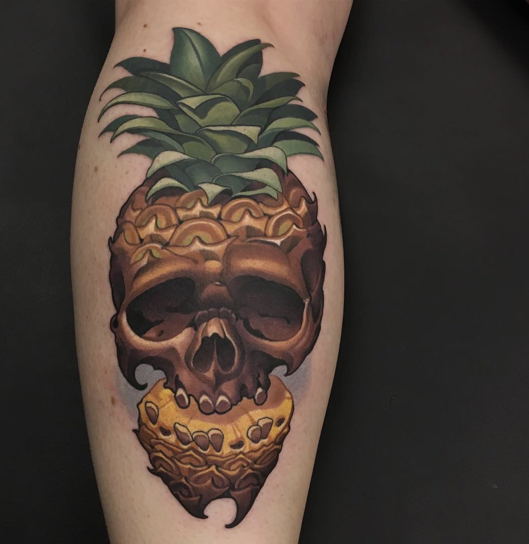 Tattoo of a pineapple skull with a snake wrapped around it on a person's arm.