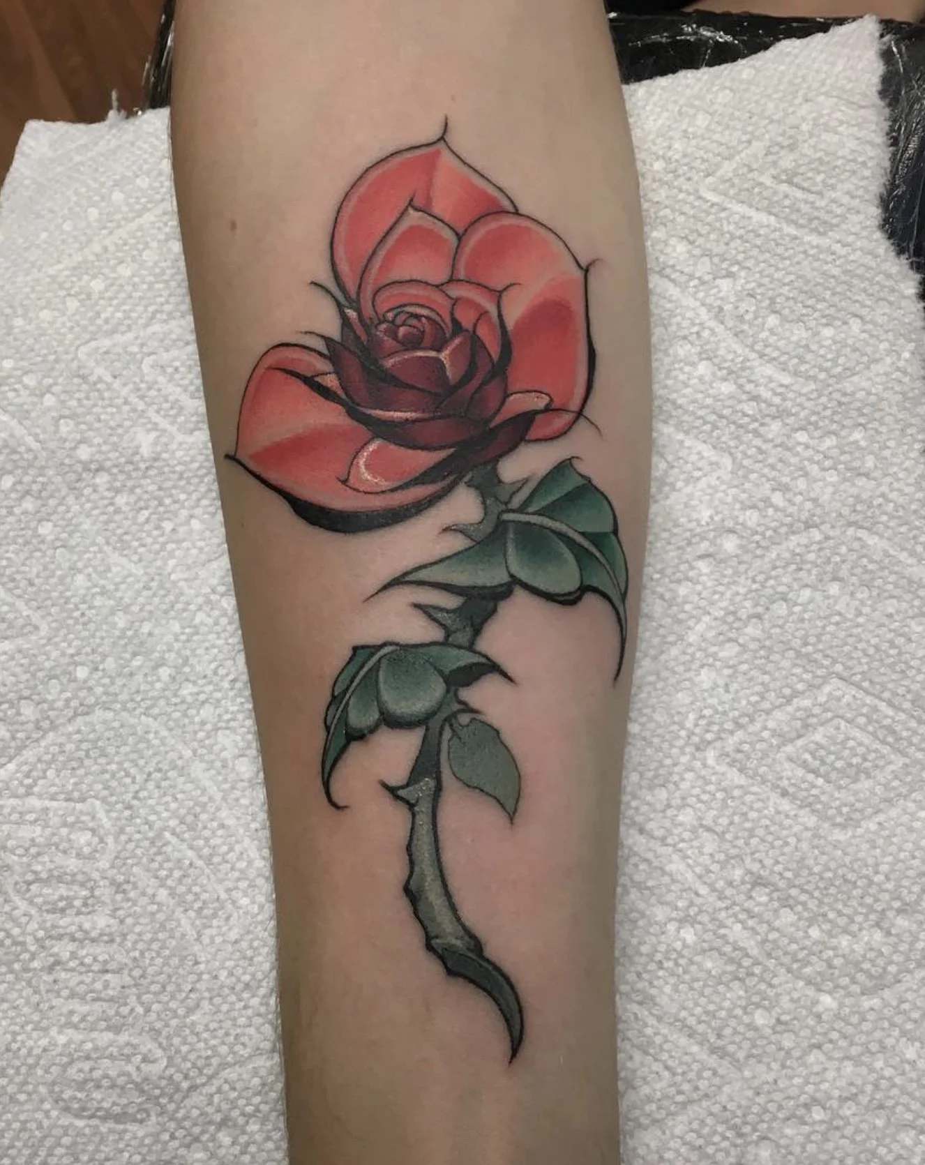 A colorful tattoo of a pink rose with green leaves on a person's arm.