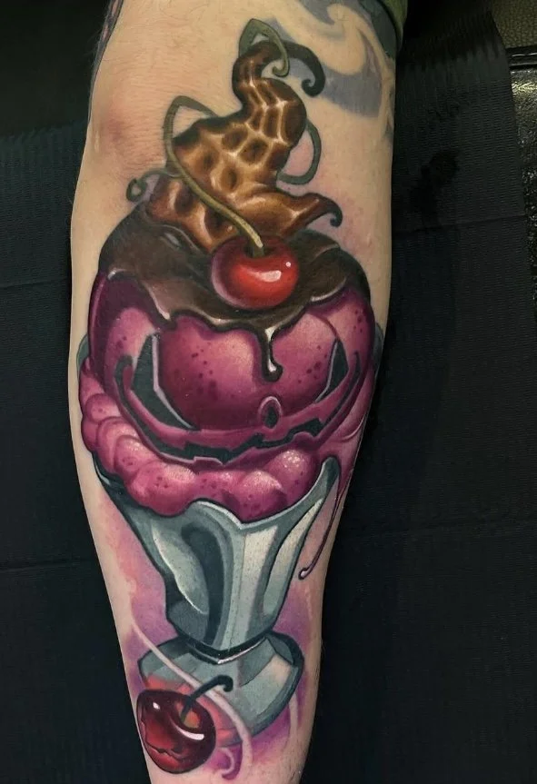 Colorful tattoo of a cherry sundae on a person's arm, featuring ice cream, chocolate syrup, whipped cream, and a cherry on top.