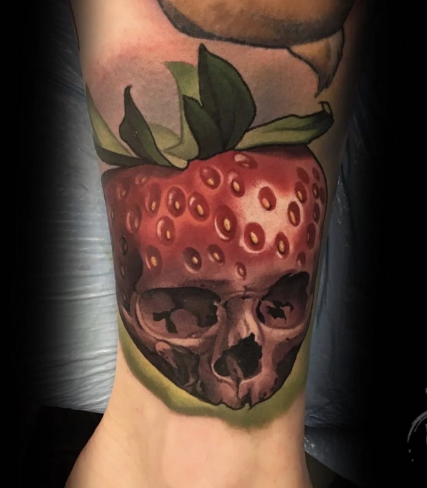 Tattoo of a strawberry with a skull at the bottom of the berry, with leaves at the top of the berry.