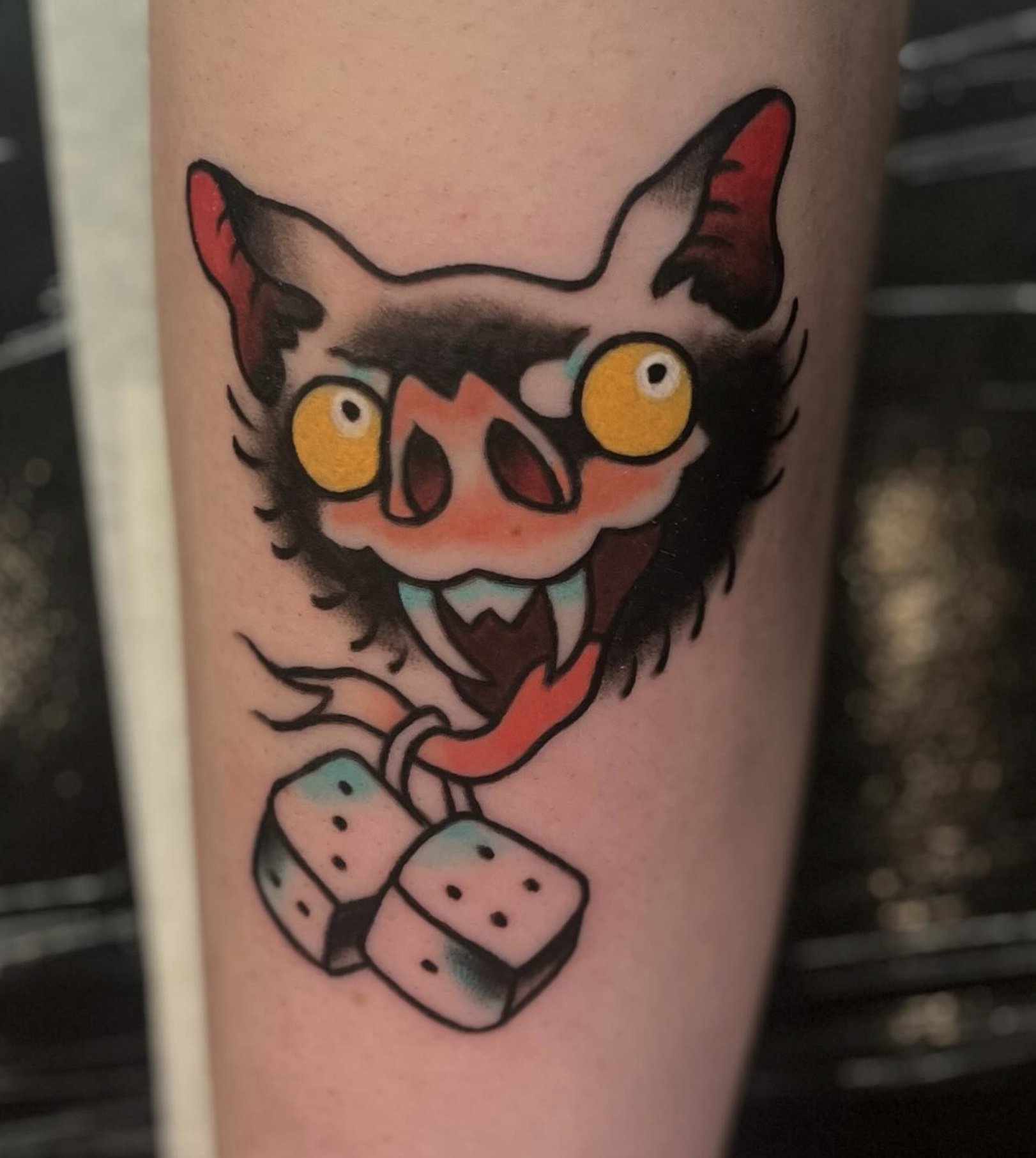 Tattoo of a cartoon devil face with large yellow eyes, sharp horns, and a mischievous smile on a person's arm.