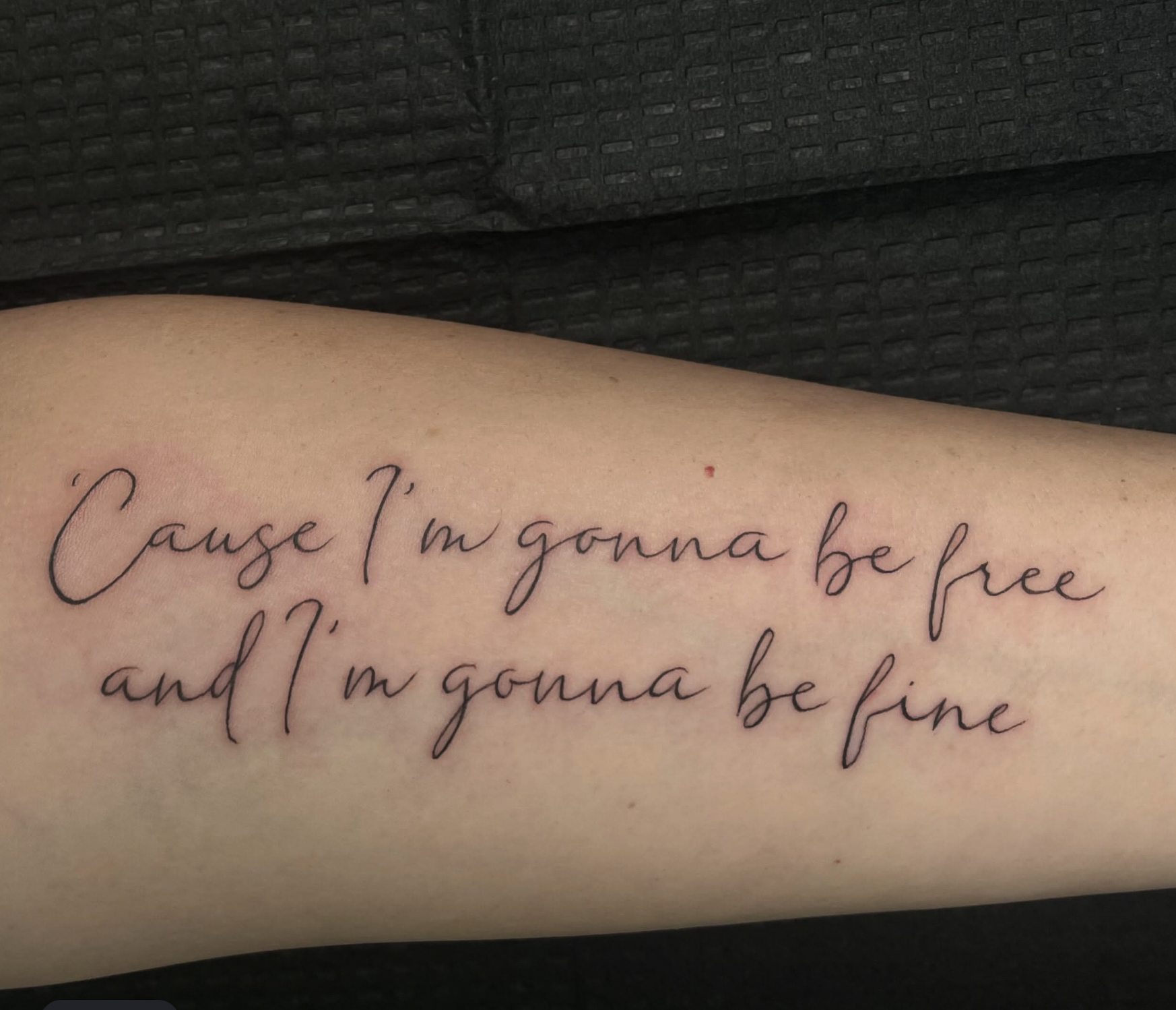 Close-up of a handwritten quote on skin that reads: "Cause I'm gonna be free and I may not be fine" with a black fabric background.