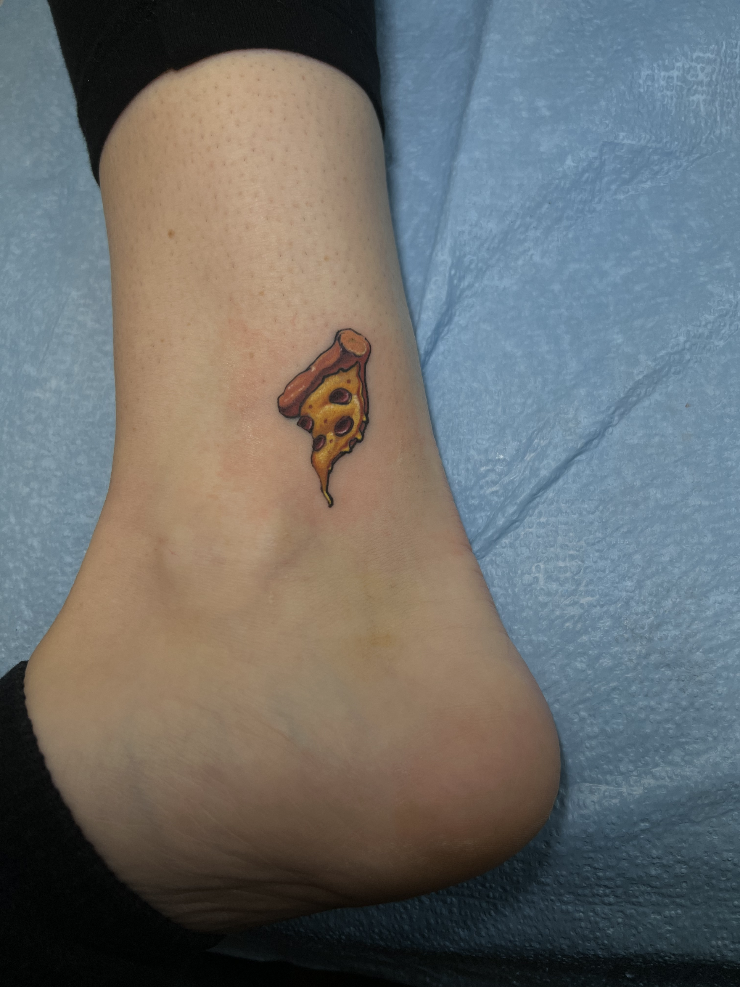Tattoo of a slice of pizza on a person's ankle.