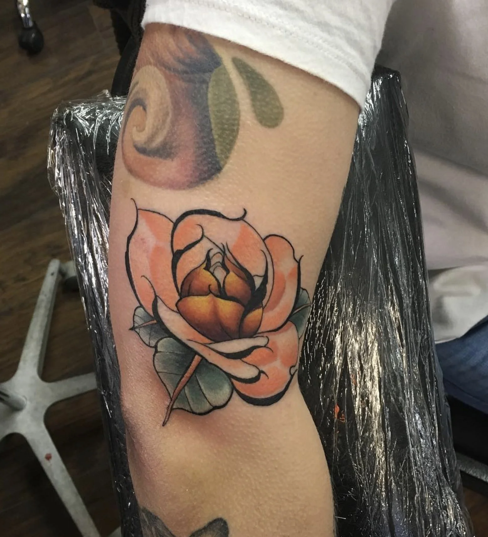 Tattoo of a flower with orange petals and green leaves on a person's forearm.