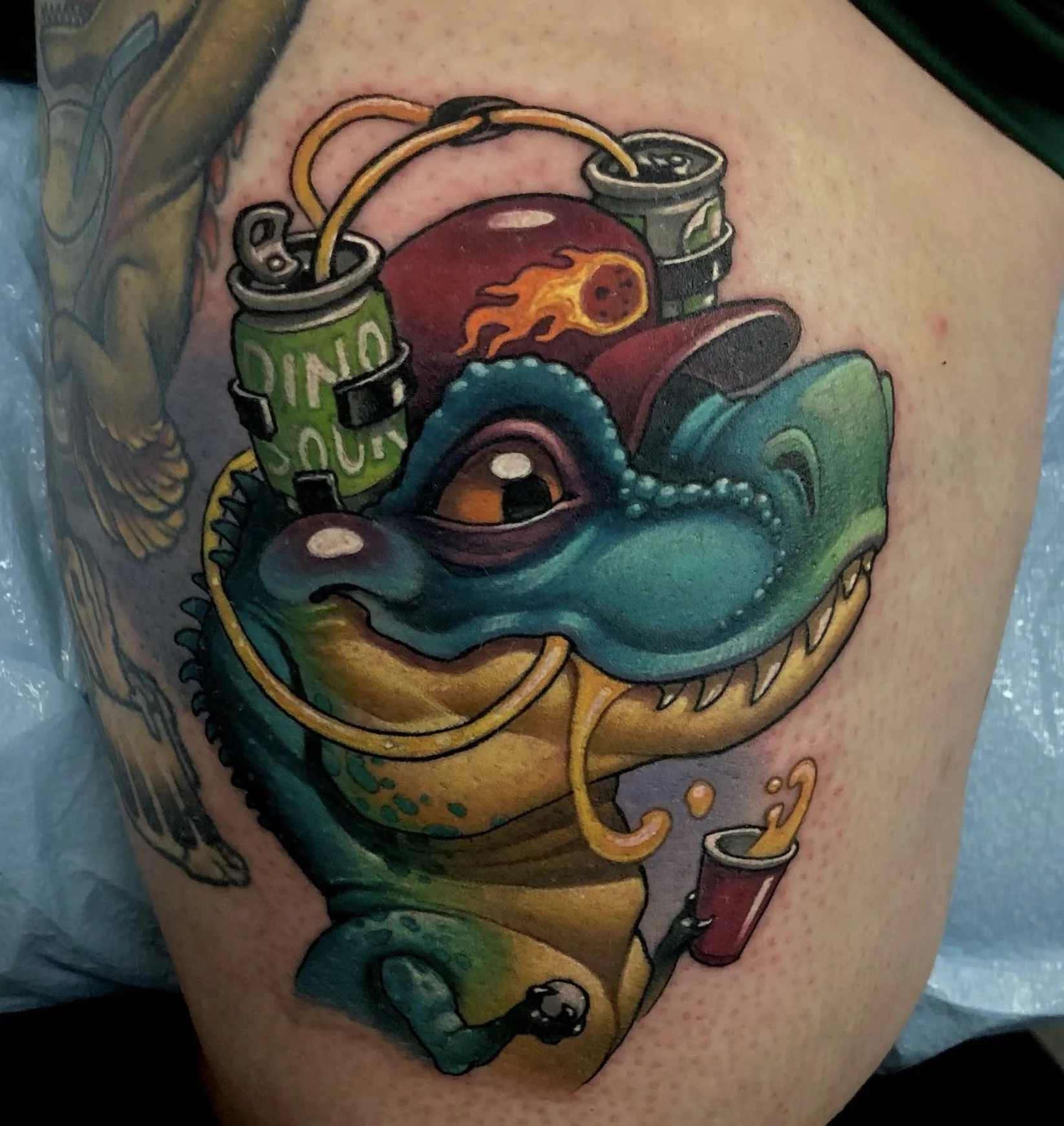 Colorful tattoo of a dinosaur holding a can of soda, with a ball of fire on its side, vintage style, on skin.